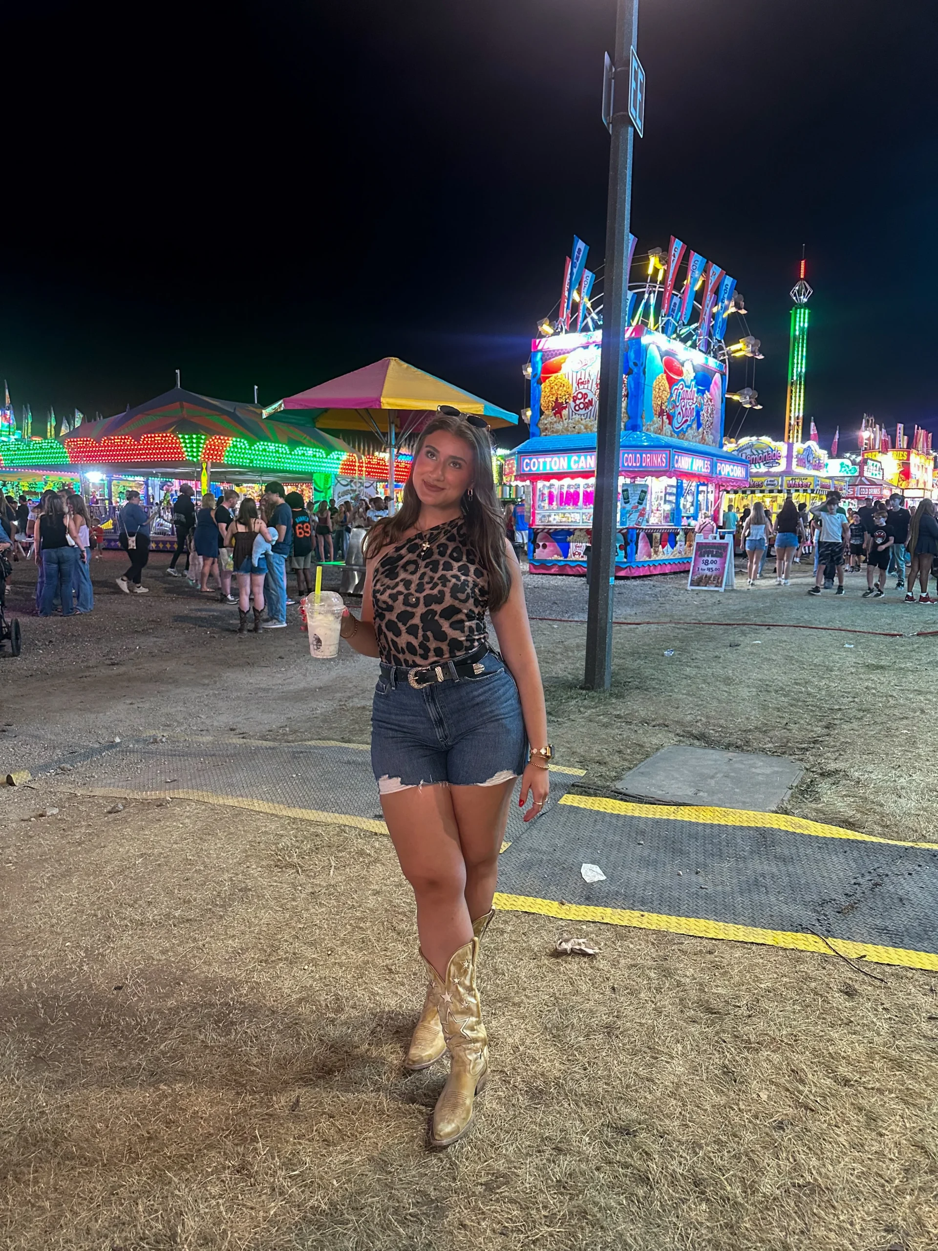 Woman in a one-shoulder leopard top, distressed denim shorts, and tall brown star-detail cowboy boots.