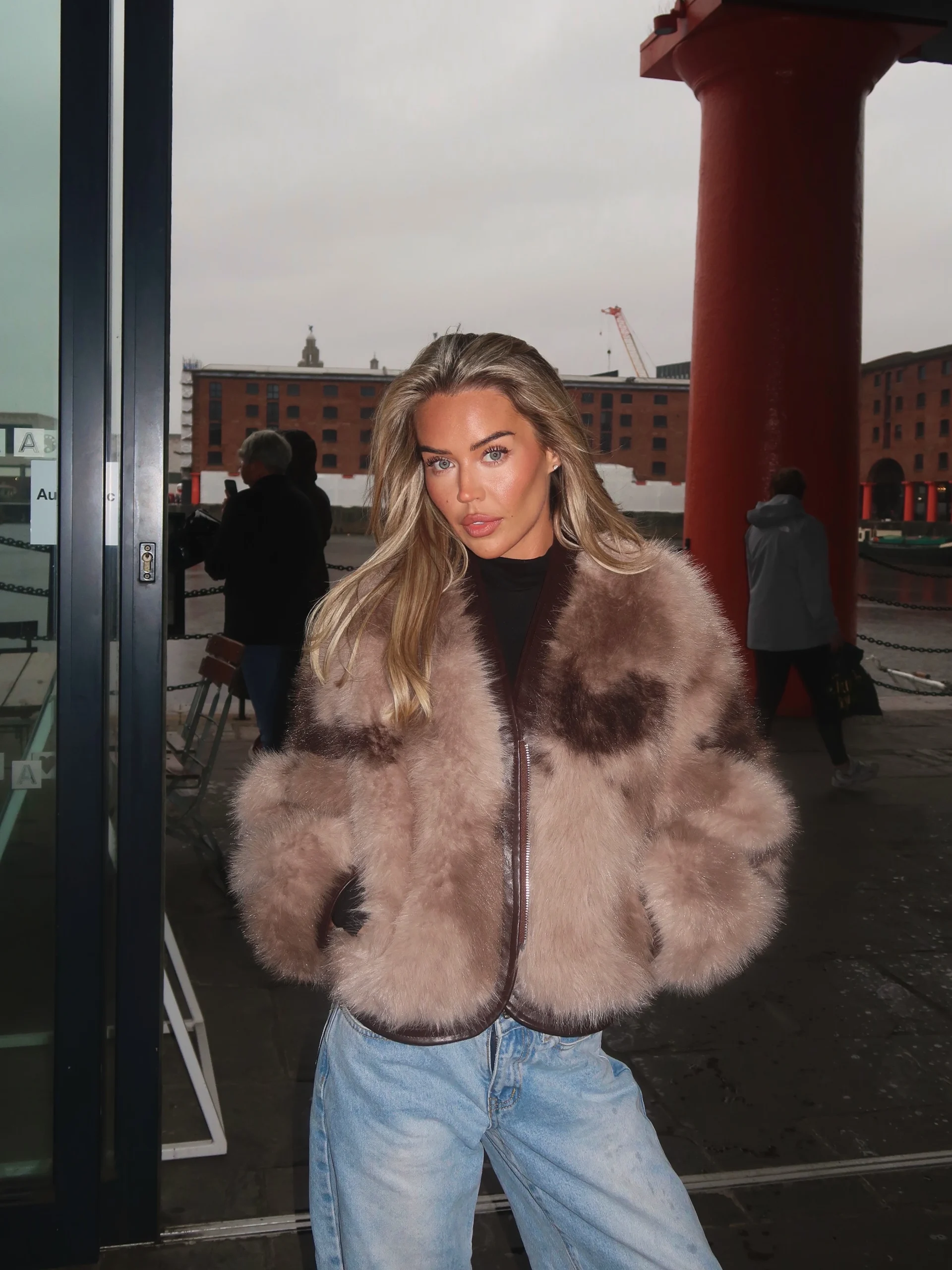 Marbled taupe faux-fur bomber jacket worn over a white tee with light-wash jeans and brown boots.