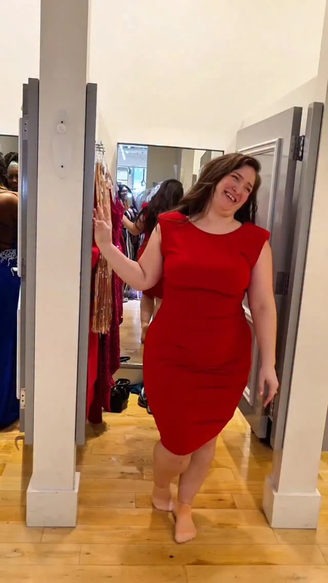 Woman in a fitted bright red cap sleeve dress standing barefoot in a fitting room.