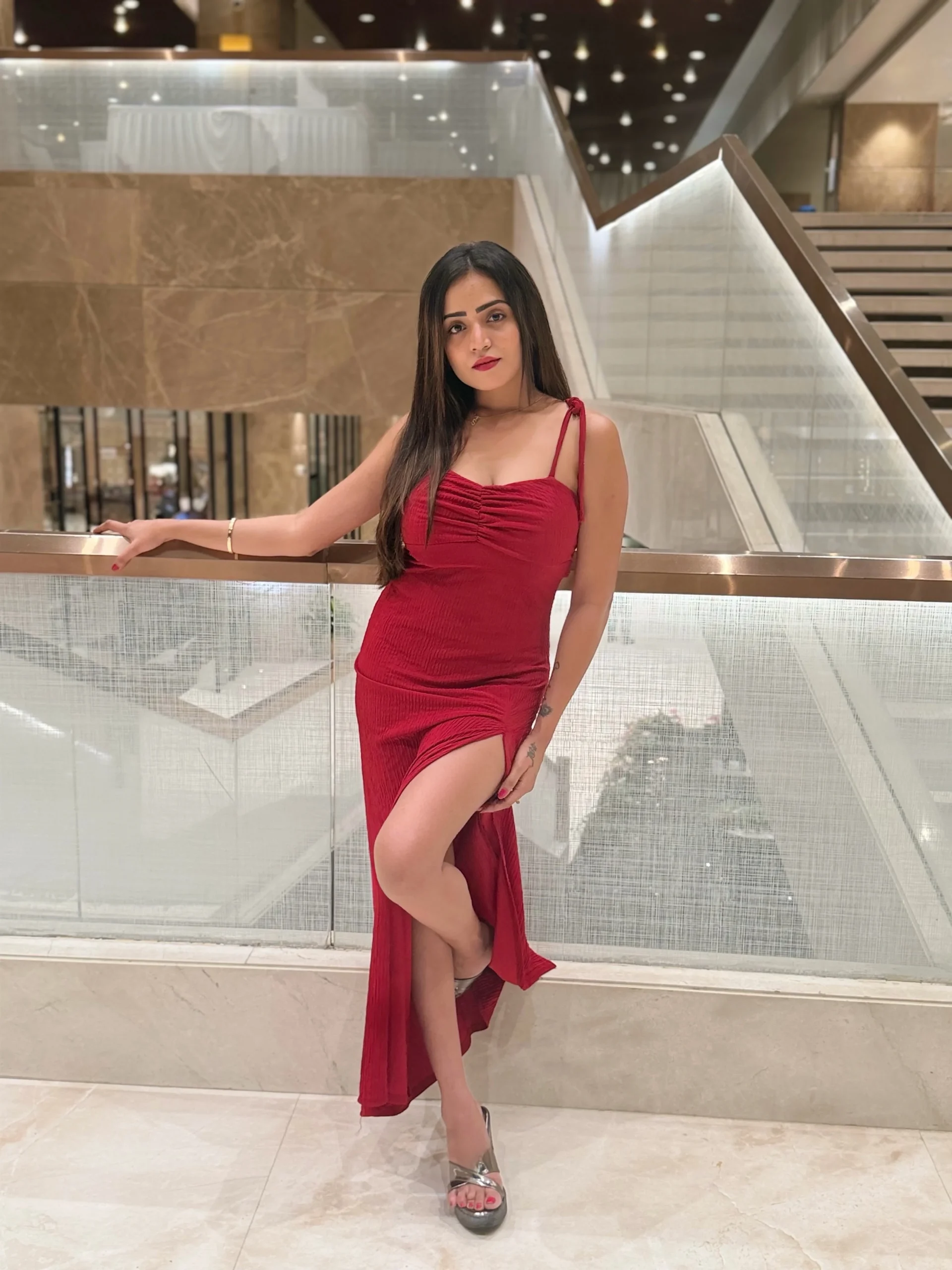 Woman in a red form-fitting maxi dress with thigh slit and metallic silver strappy heeled sandals.