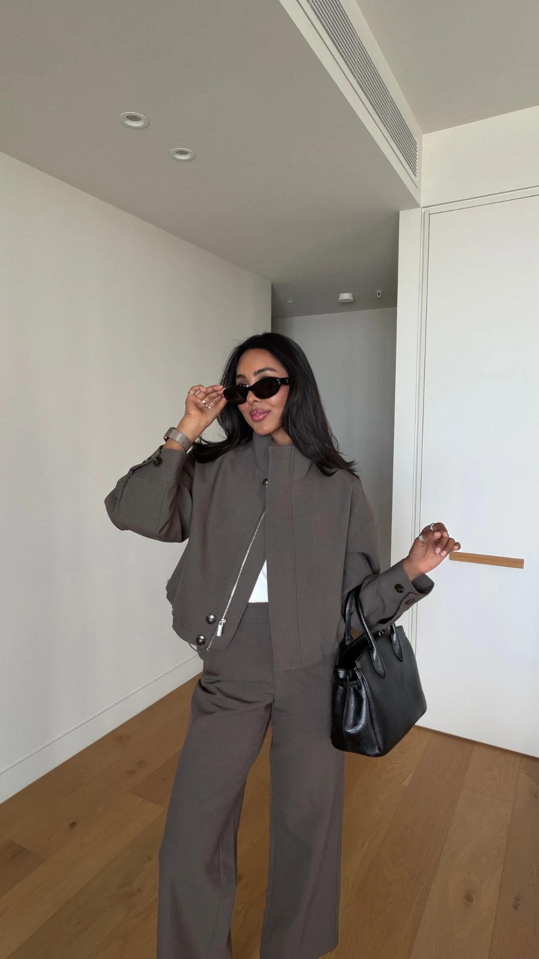 Woman in a taupe-gray matching funnel-neck cropped jacket, wide-leg trousers, and black heels.
