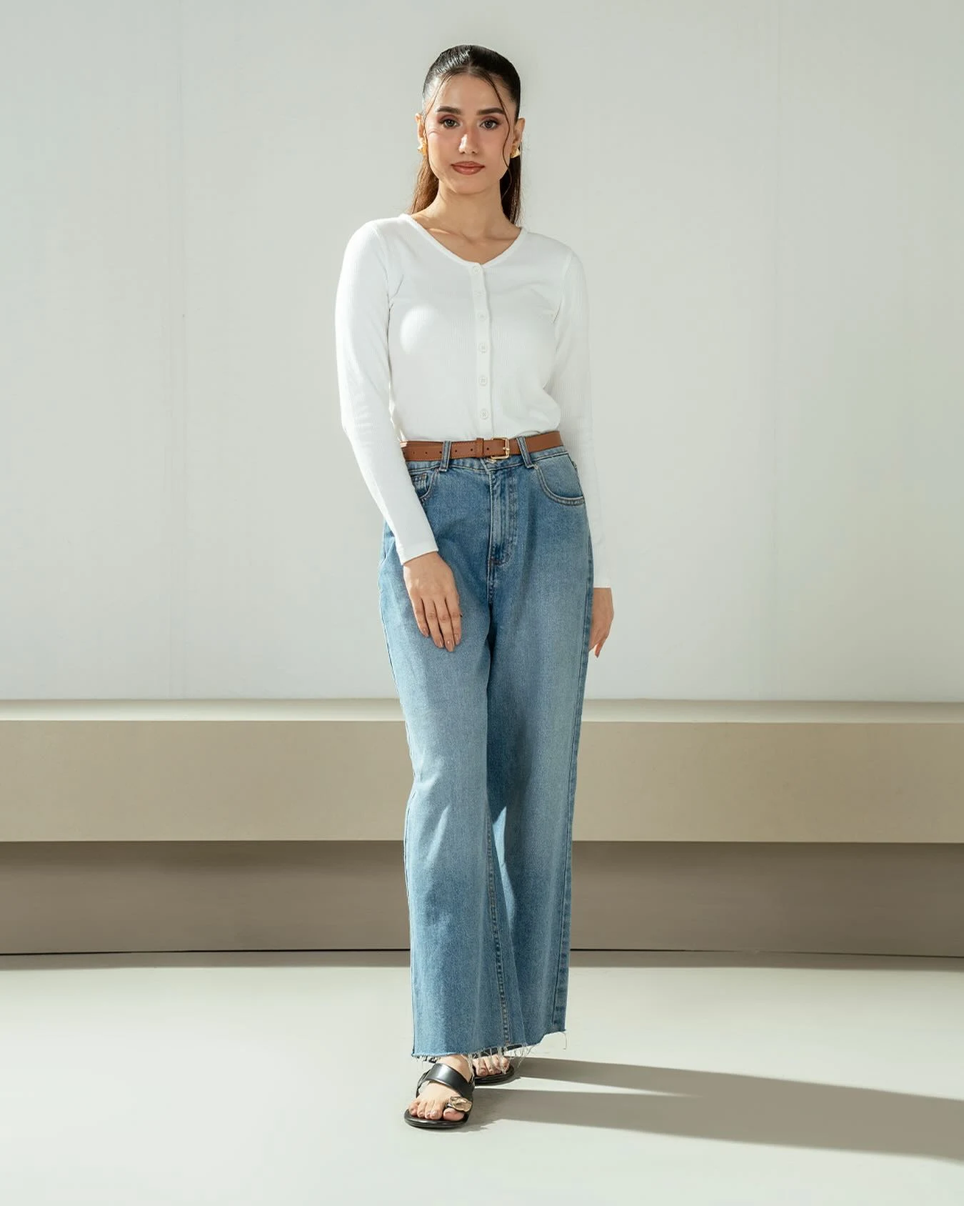 White ribbed cardigan and wide-leg jeans belted at the waist with black flat sandals.
