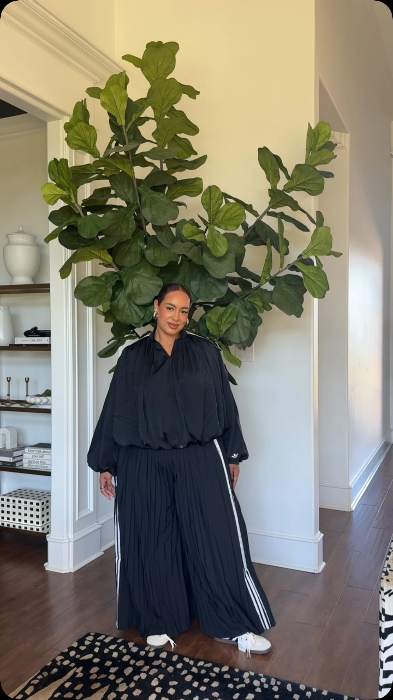 Person in voluminous black blouse and wide pleated black trousers with white stripe detail and white shoes.