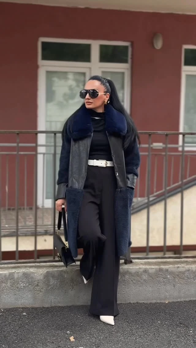 Black turtleneck and wide-leg trousers layered under a leather and navy fur-trim coat with white heels.