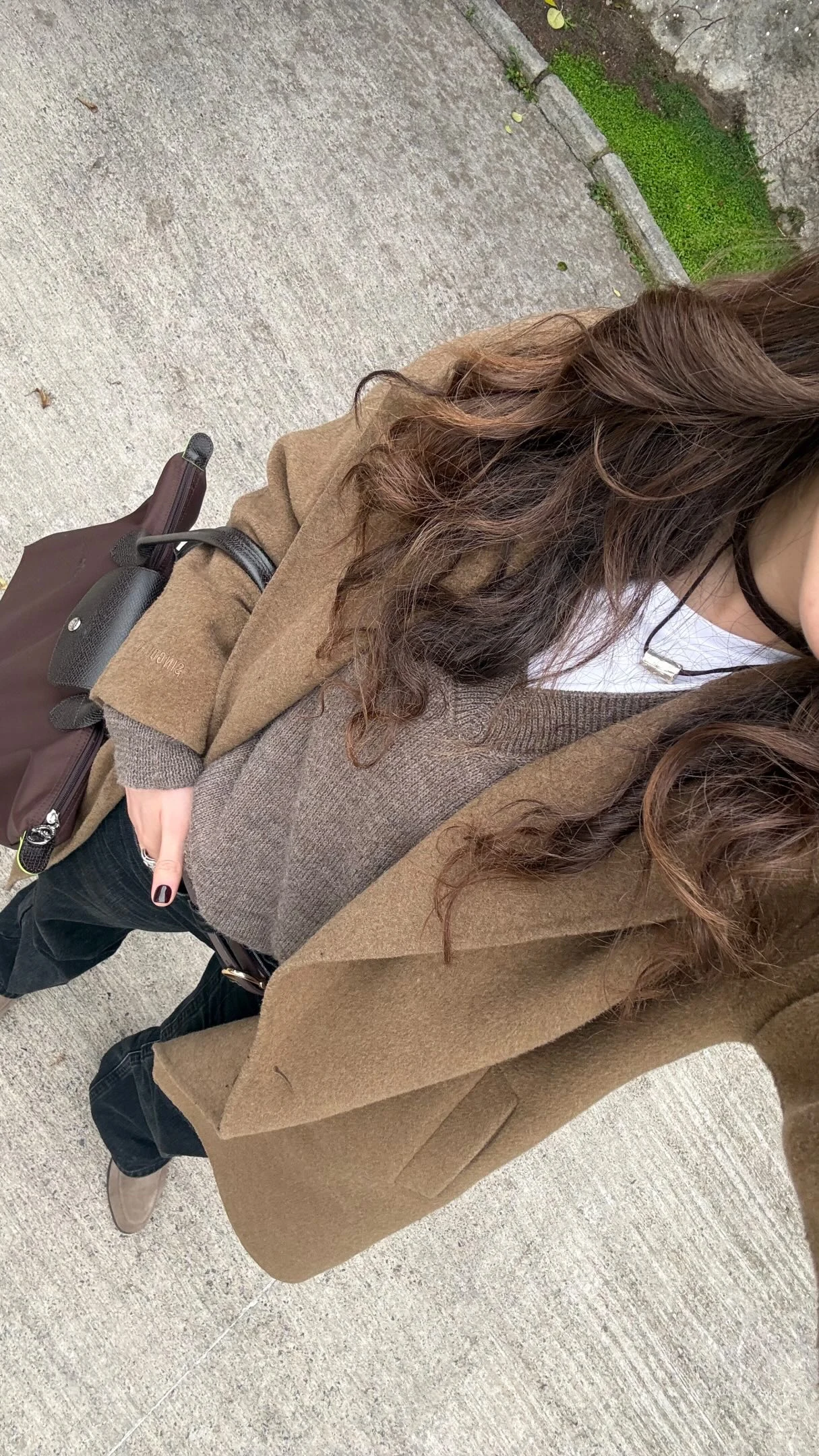 Person wearing a black wool coat, grey knit top, blue wide-leg jeans, gold belt, and white sneakers.