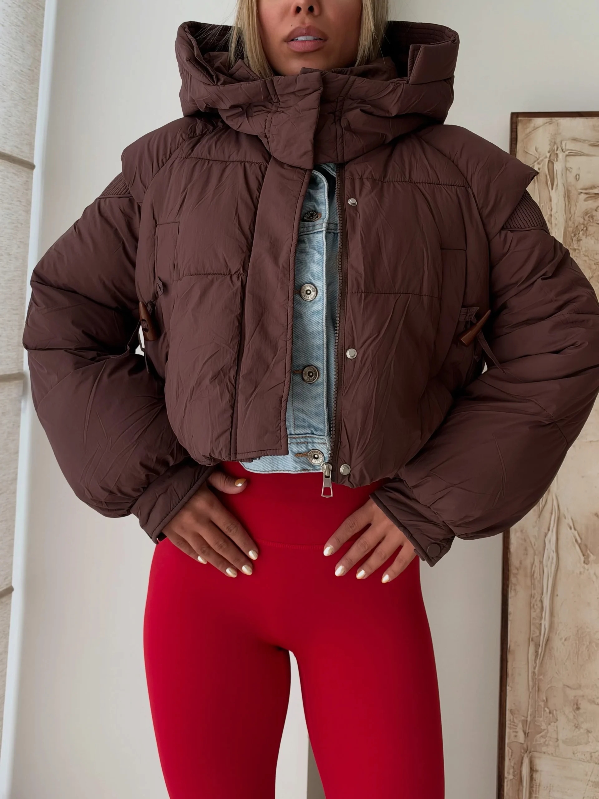Dark brown cropped puffer jacket layered over a light blue denim jacket with bright red leggings.