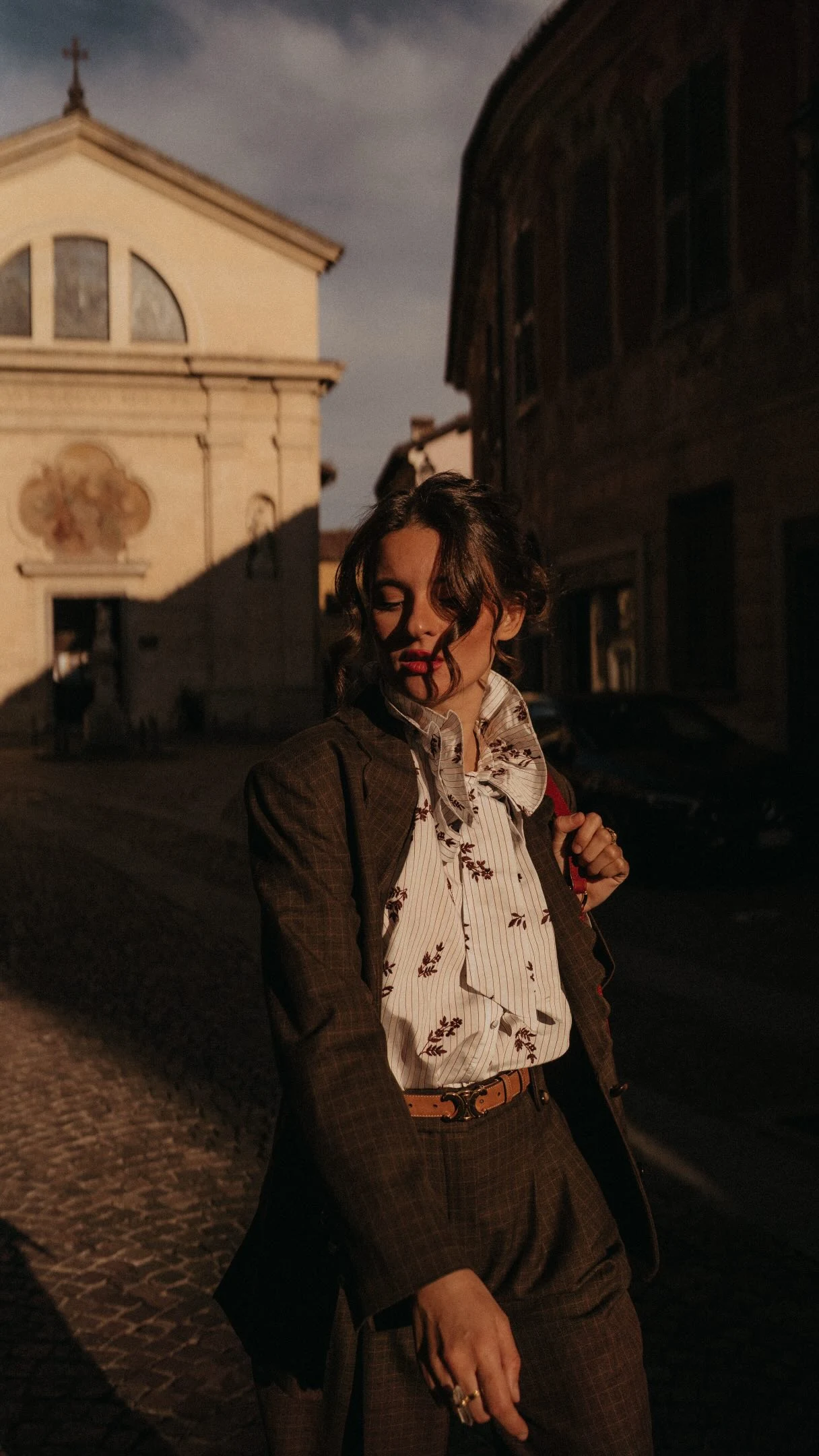 Brown plaid blazer and trousers paired with a white ruffled floral blouse and tan belted waist.