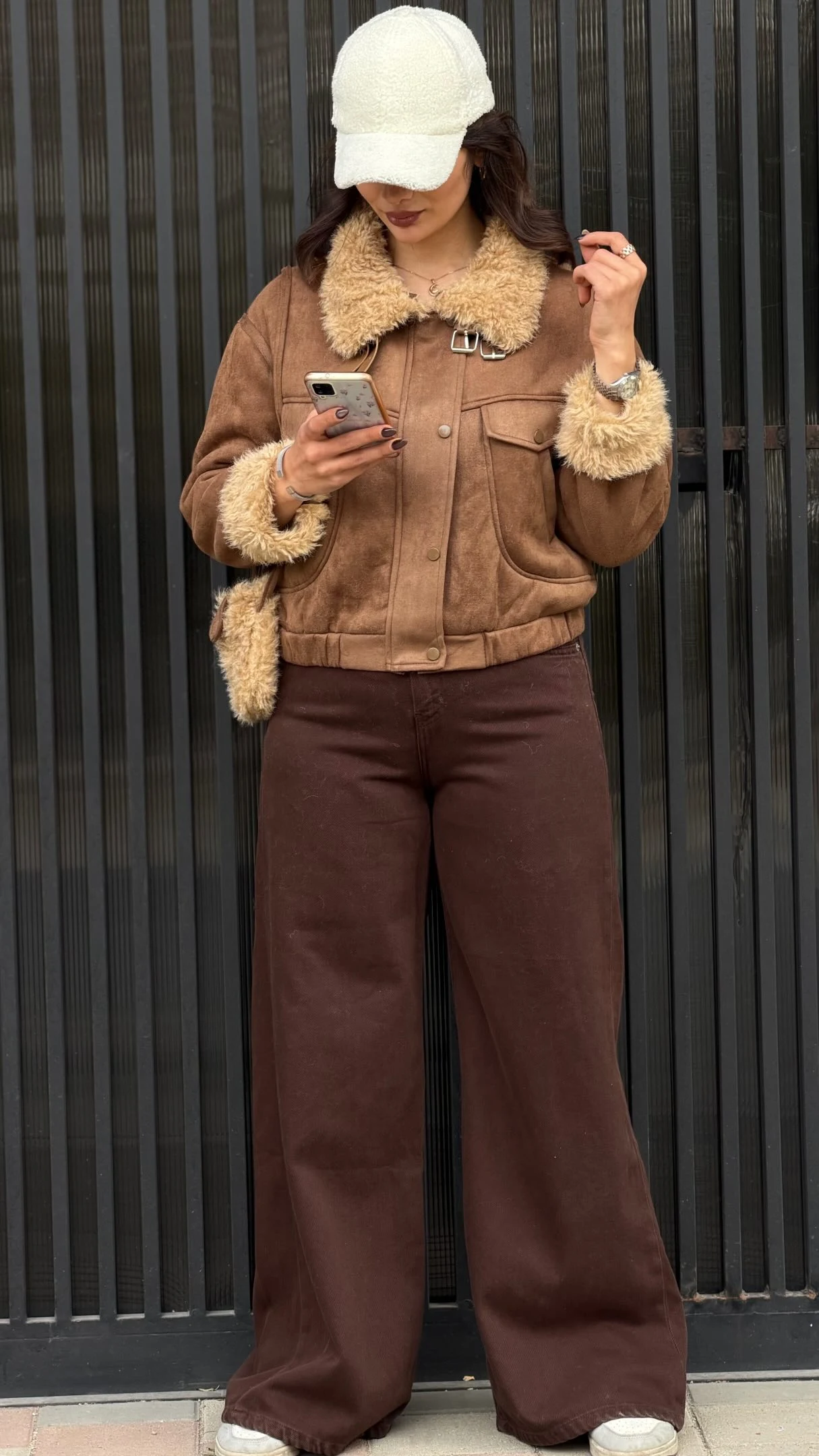 Cropped brown shearling jacket with tan collar over wide-leg dark pants and light sneakers.