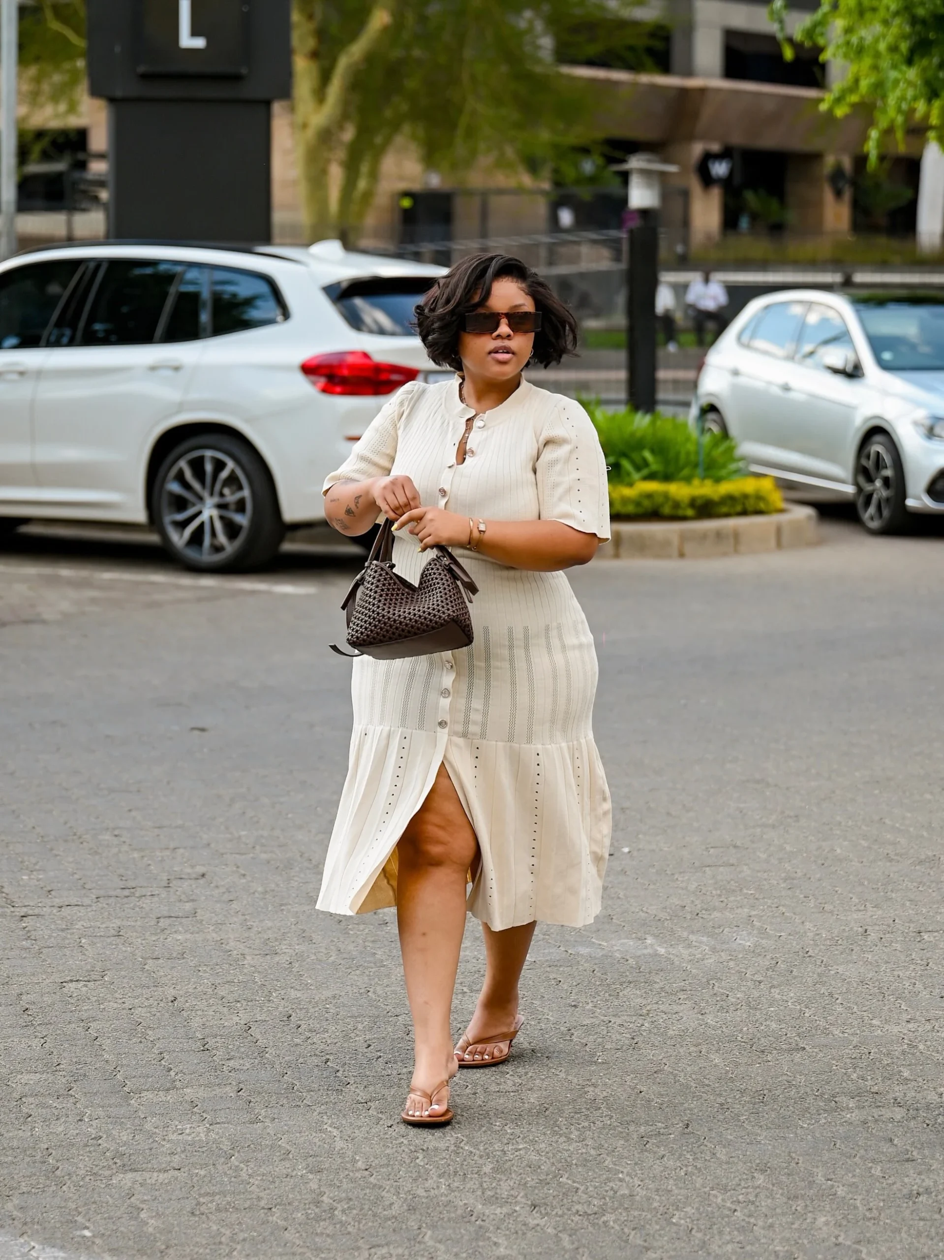 Cream button-front midi dress with flared skirt, woven handbag, and flat open-toe sandals.