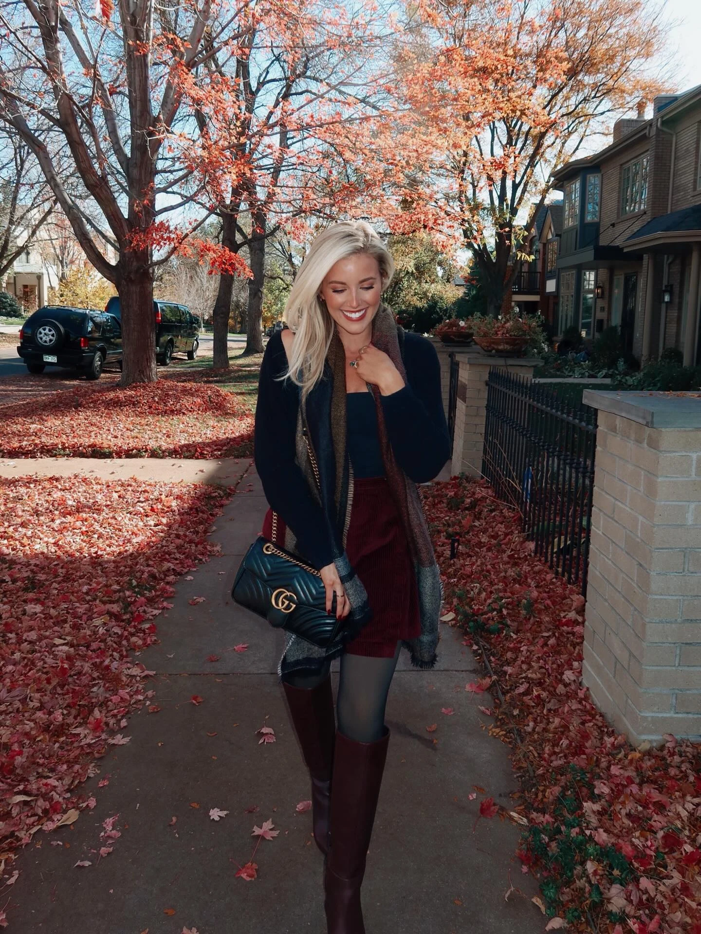 Dark navy sweater over matching square-neck top, maroon corduroy mini skirt, sheer black tights, tall burgundy leather boots, black quilted shoulder bag, and patterned scarf