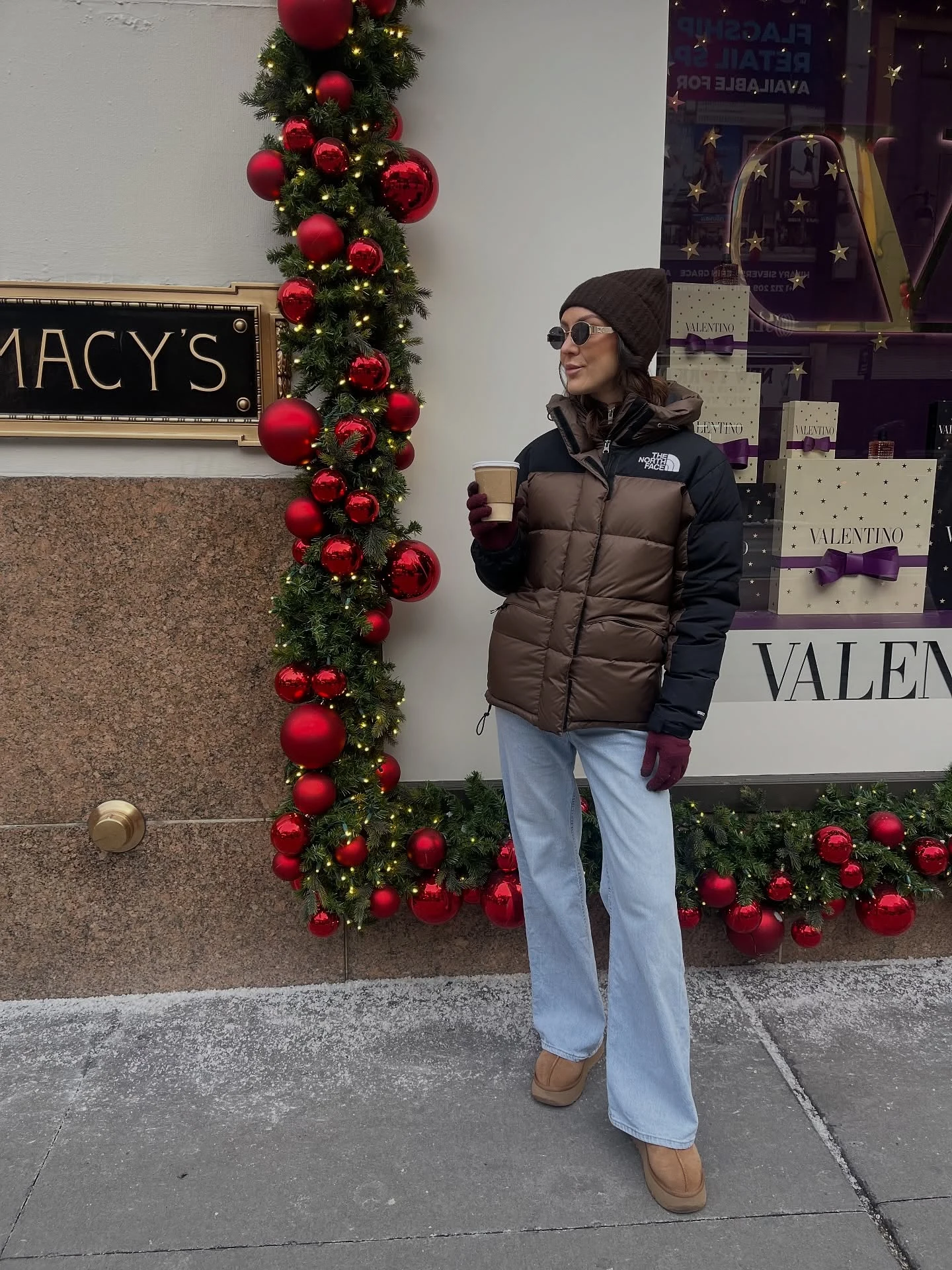 Person wearing a brown puffer coat, wide-leg jeans, tan platform UGG boots, and maroon gloves.
