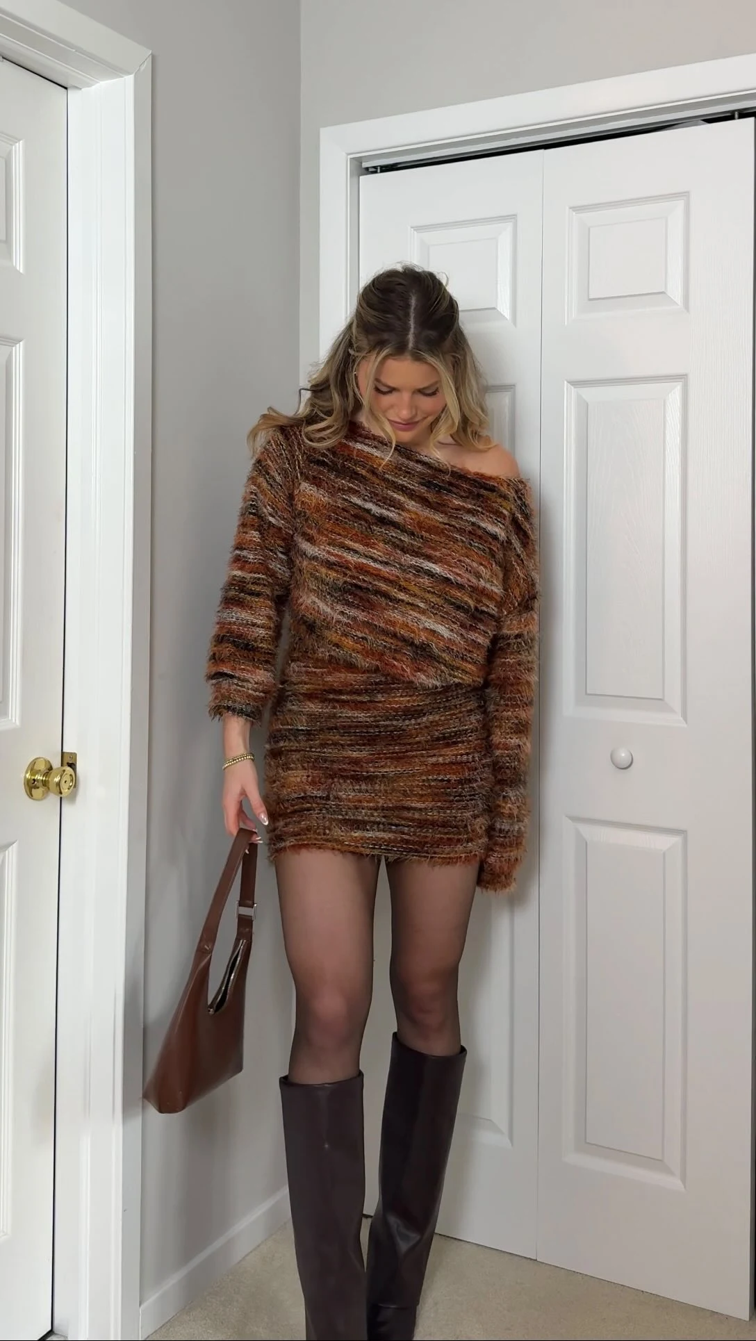 Fuzzy off-shoulder sweater dress in brown and rust tones with dark boots, tights, and a structured handbag.