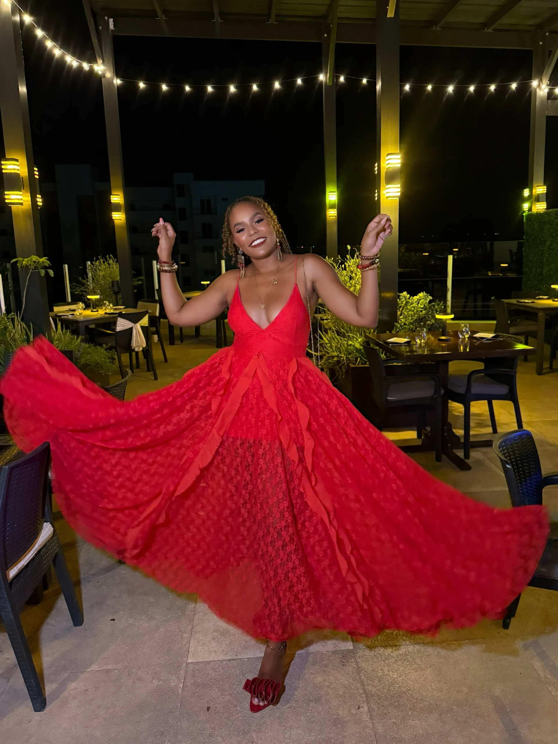 Woman wearing a bright red floor-length lace dress with a plunging neckline and red ruffled heels.