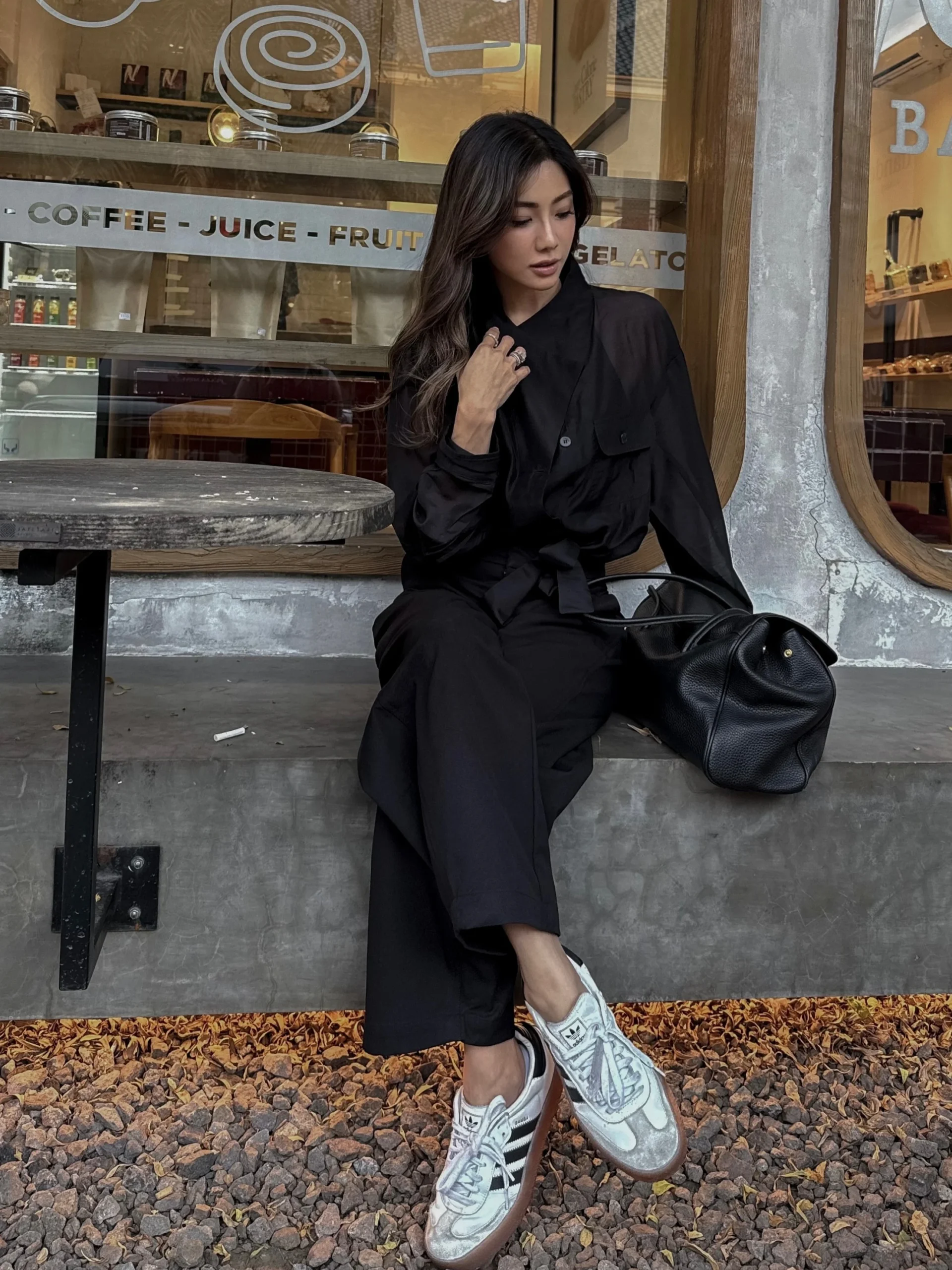 Sheer black overshirt, wide-leg trousers, white Adidas Sambas, and black leather tote bag.