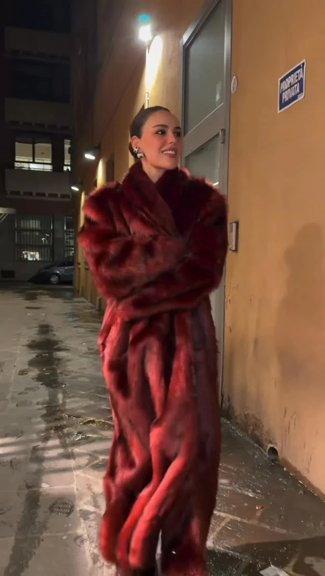 Woman in a short black dress, floor-length burgundy faux fur coat, and large gold hoop earrings.