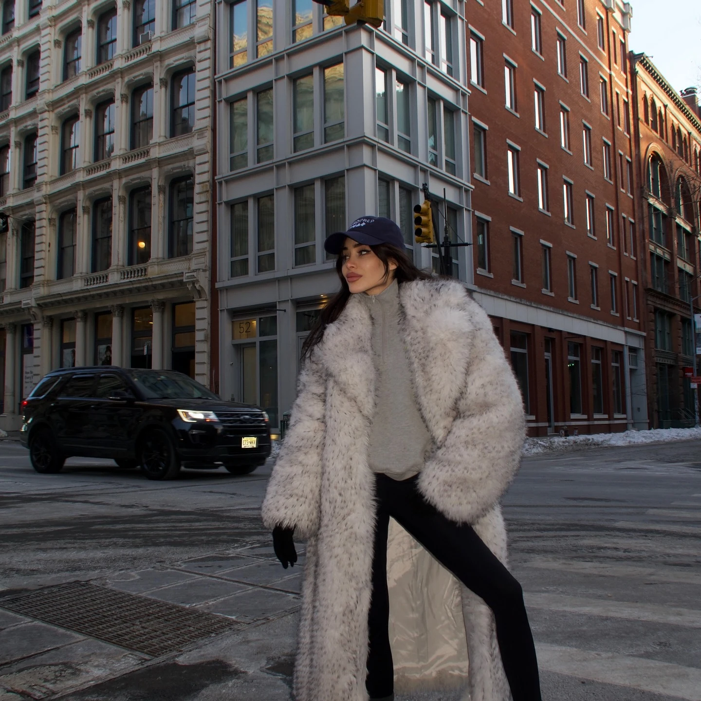 White speckled faux-fur coat styled with gray turtleneck, black leggings, and a navy baseball cap.