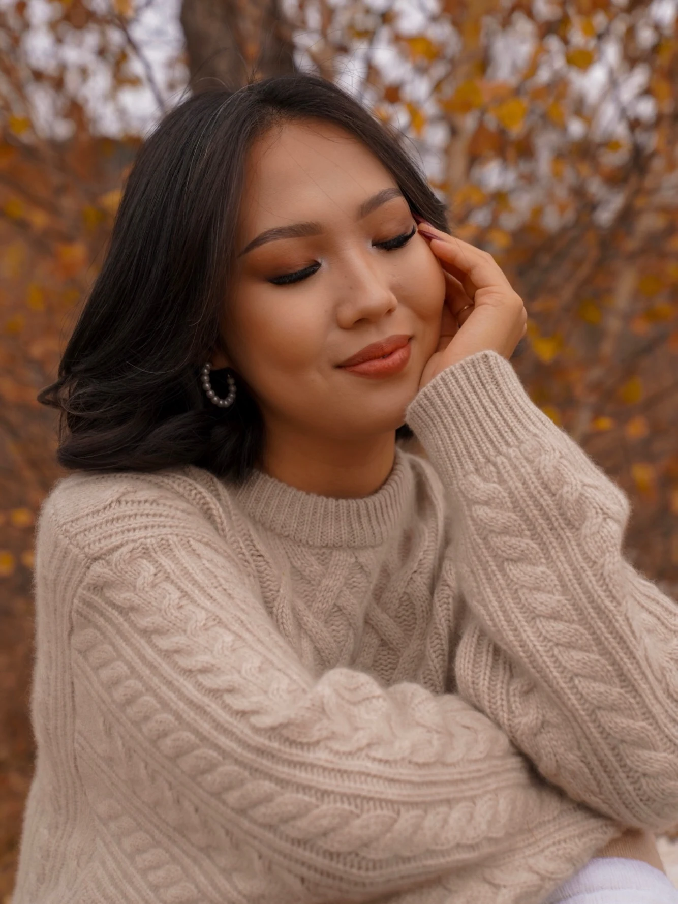 Beige cable knit sweater with white shorts, knee-high black boots, pearl hoops, and a sunflower bouquet.