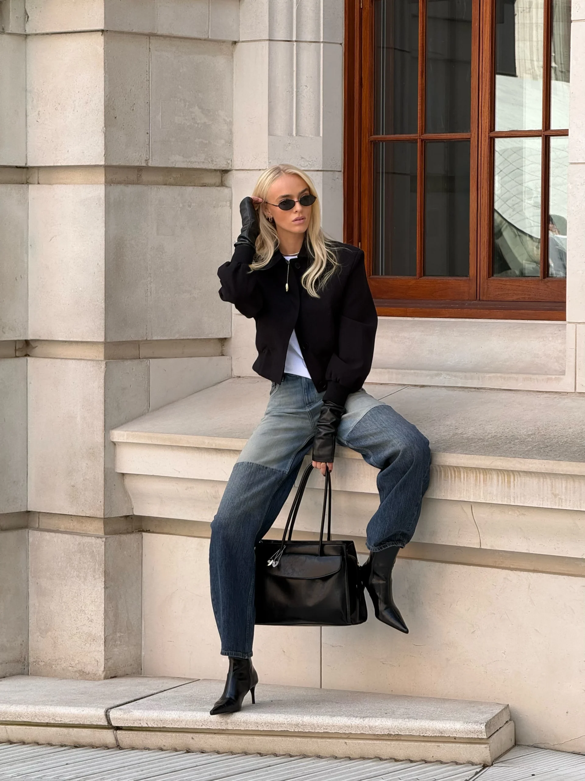Cropped black jacket with puffy sleeves over white top, loose blue jeans, black boots and long gloves.