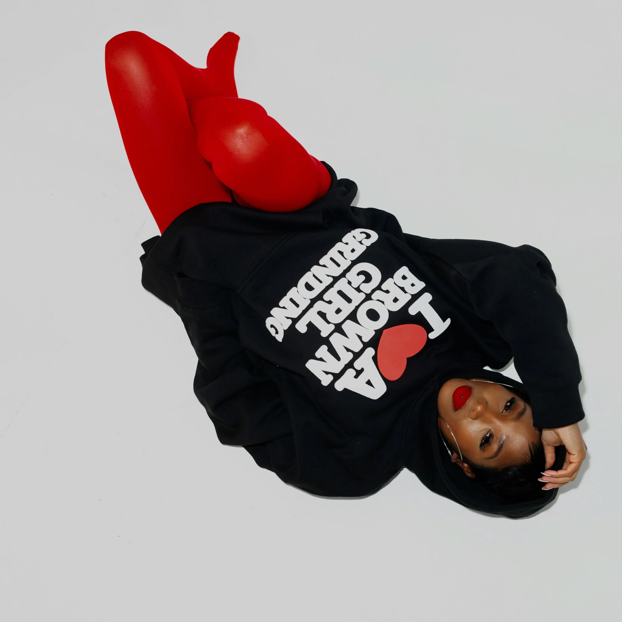 Person in an oversized black graphic hoodie with hood up, paired with bright red pants.