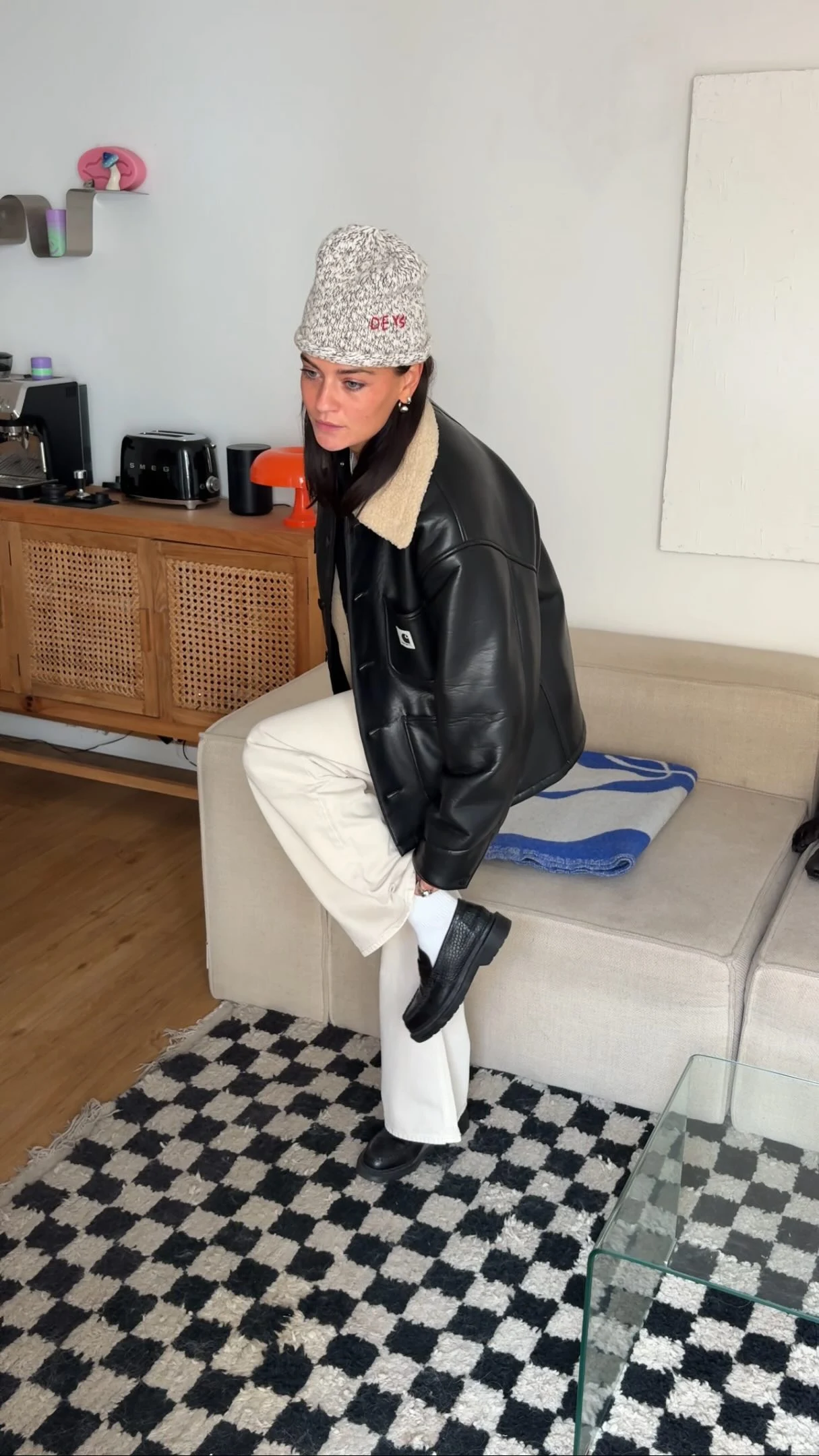 Black leather jacket over a gray sweater paired with cream wide-leg pants and black sneakers.