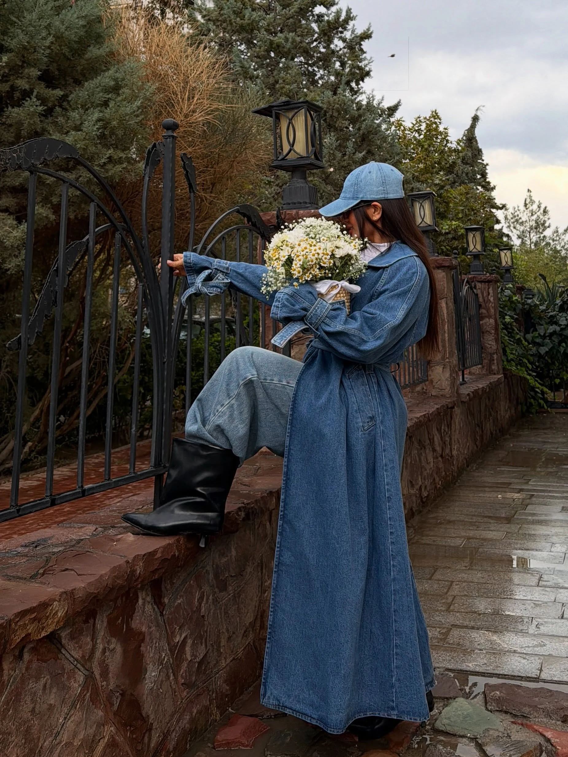 Blue denim trench coat over white top, wide-leg jeans, black boots, and a light-blue baseball cap.