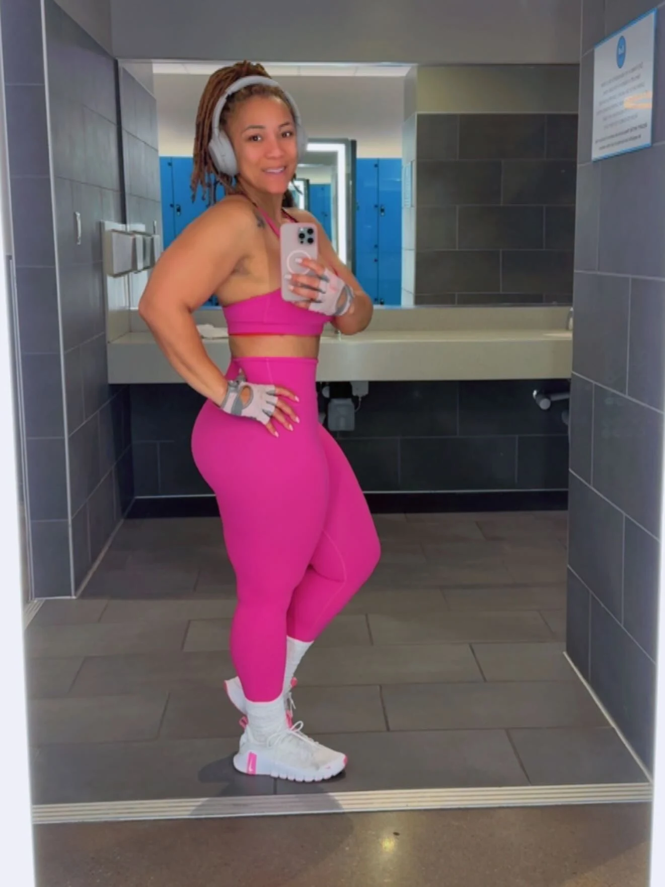 Bright pink matching sports bra and leggings with white shoes, gray gloves, and over-ear headphones.