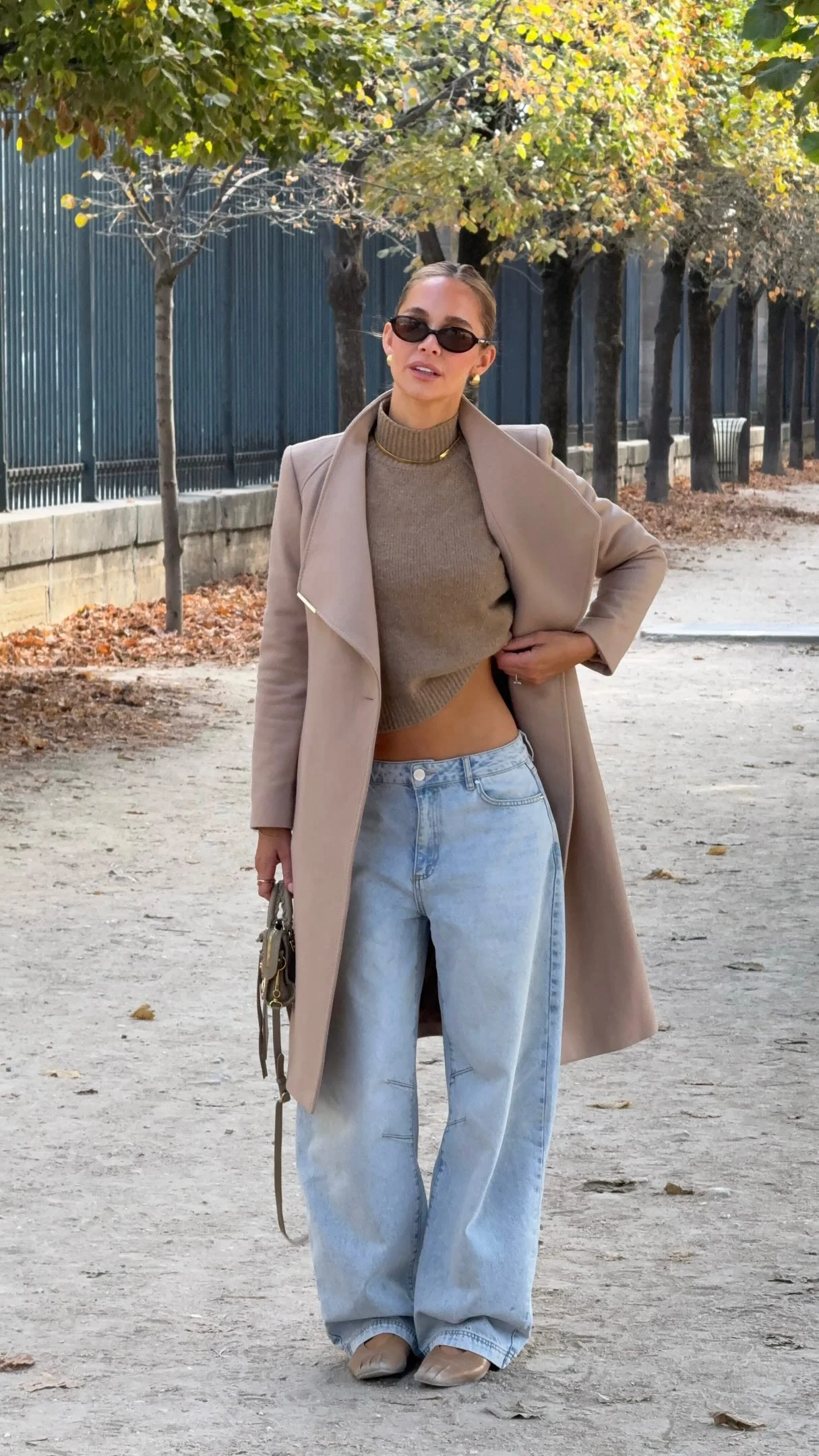 Woman wearing a camel wrap coat, ribbed turtleneck, wide-leg jeans, tan flats, and a structured handbag.