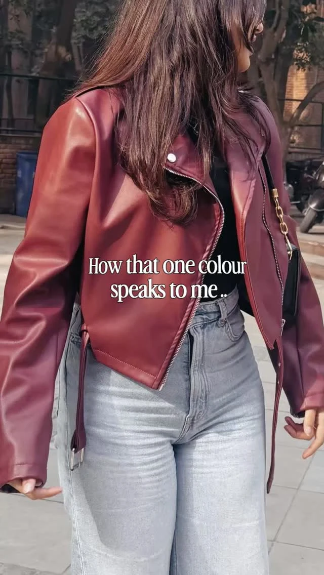 Person in a cropped cherry red jacket with silver snaps over a black top and light-wash straight jeans.