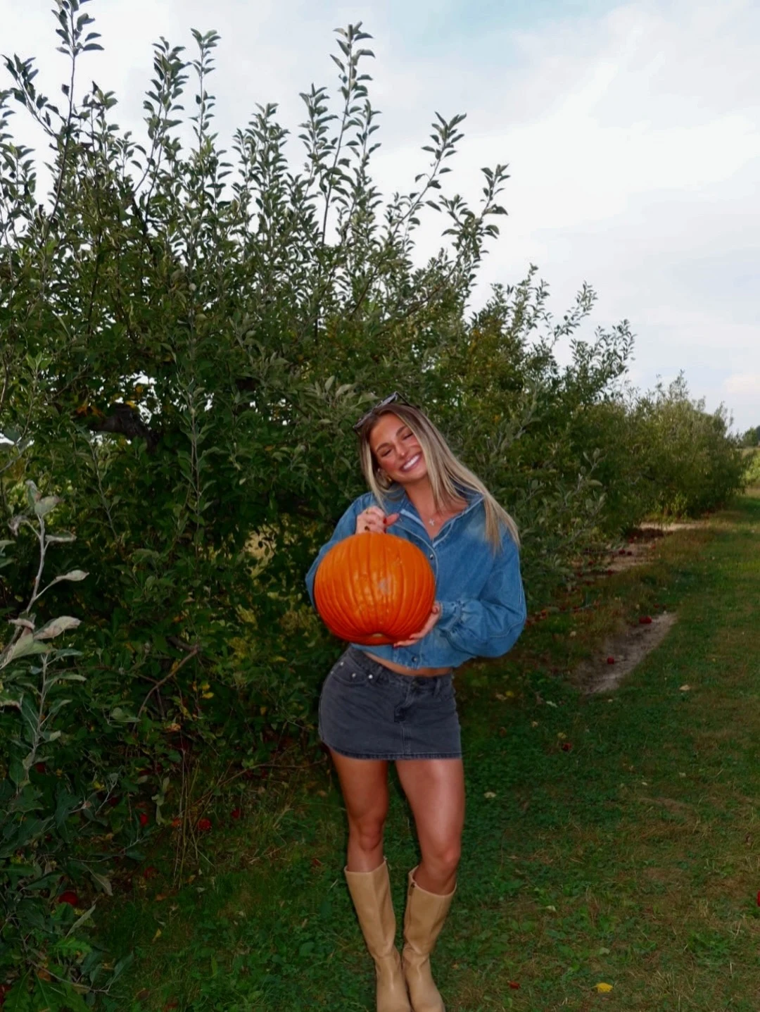 Woman wearing a cropped denim shirt, dark denim mini skirt, and tan knee-high boots at a fall fair.