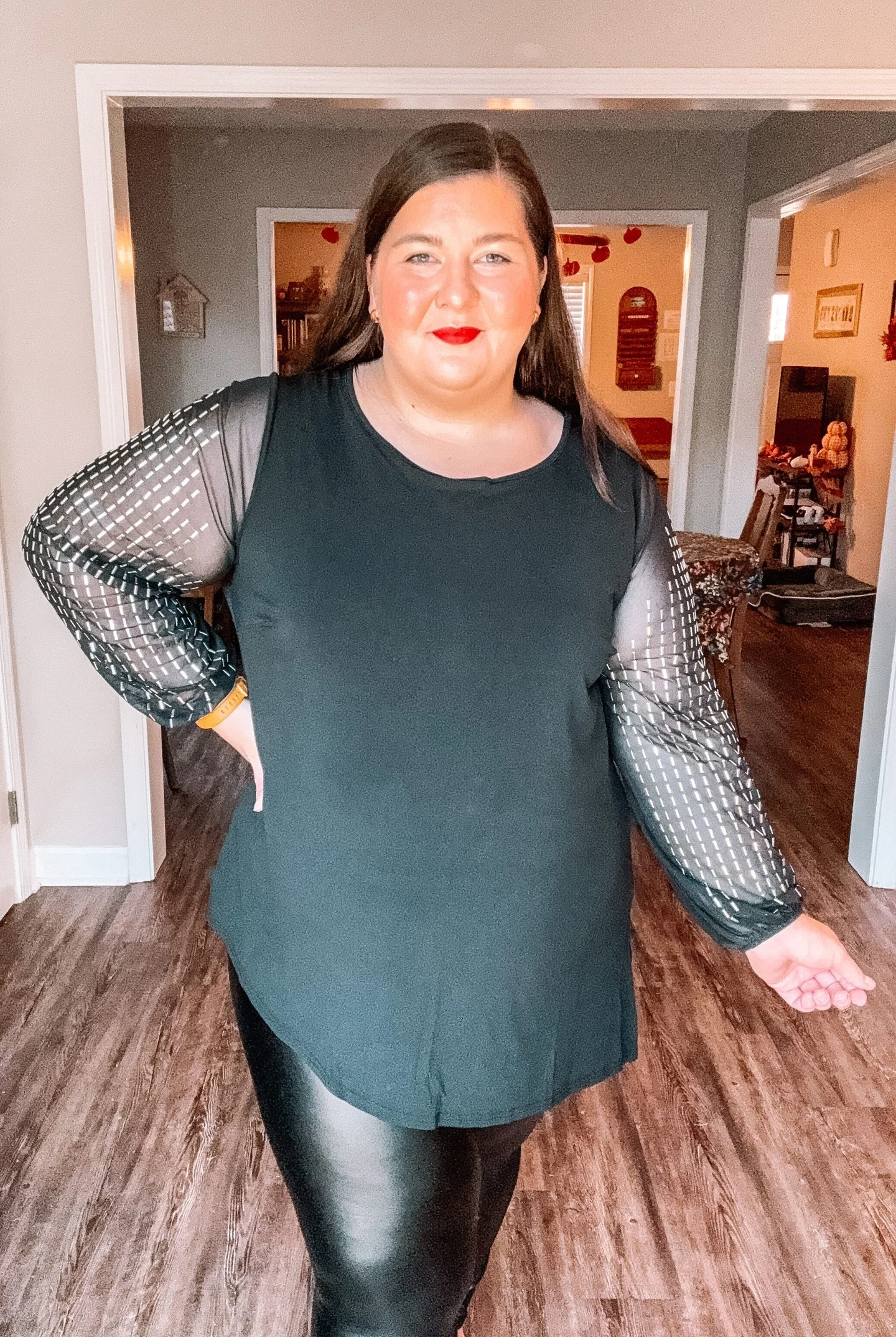 Woman in a dark teal tunic with sheer grid-patterned sleeves paired with fitted black leggings.