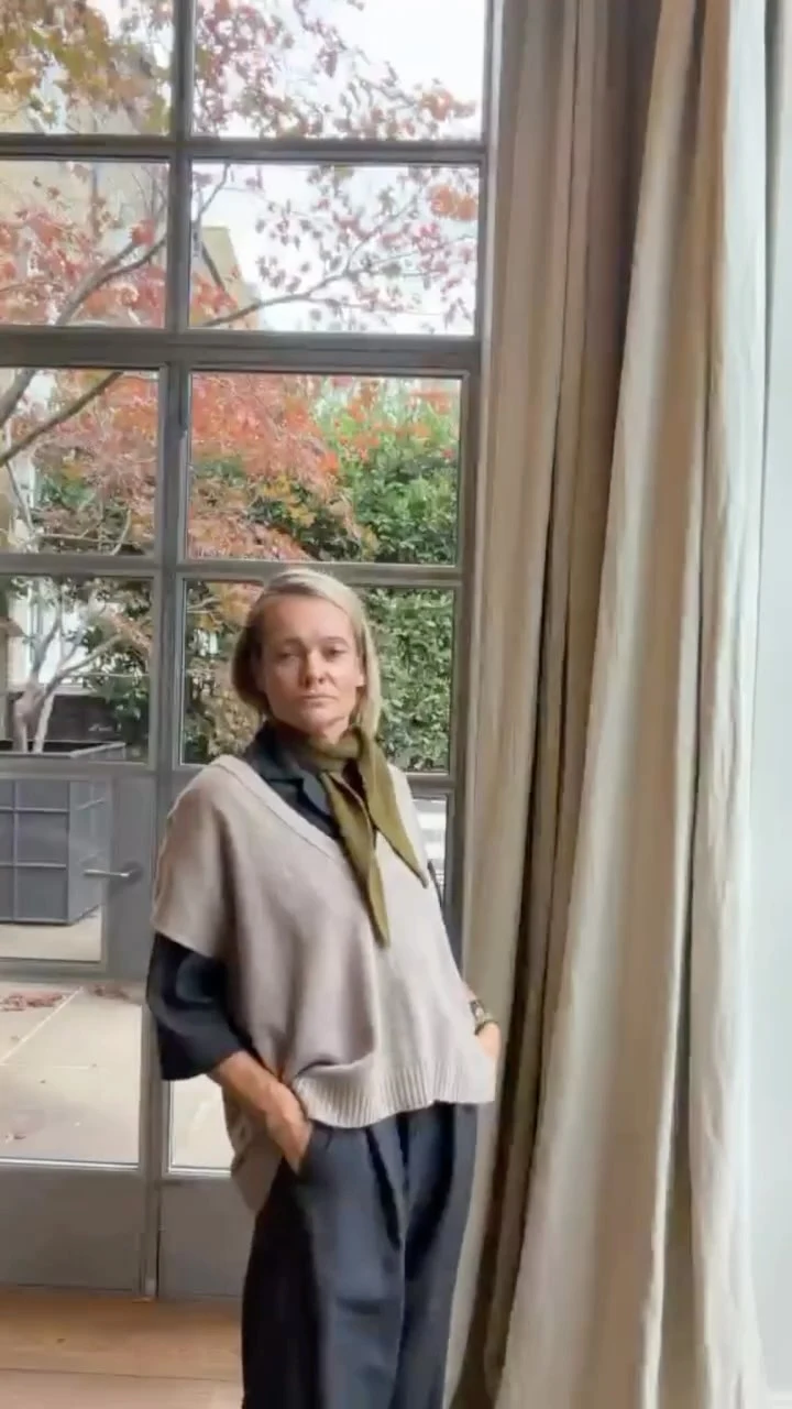 Beige sweater vest over a dark long-sleeve top with wide-leg trousers and an olive neck scarf.