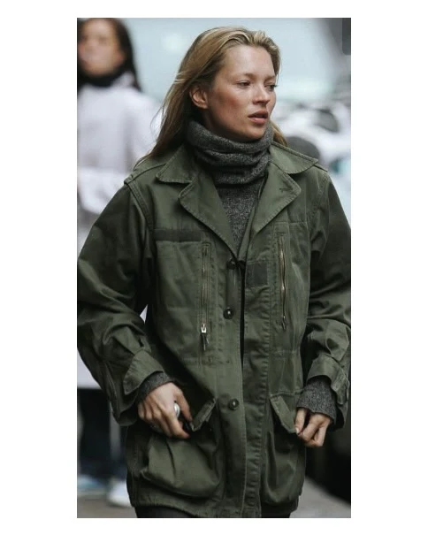 Long olive utility coat with notched collar worn over a dark gray knit top in a relaxed silhouette.