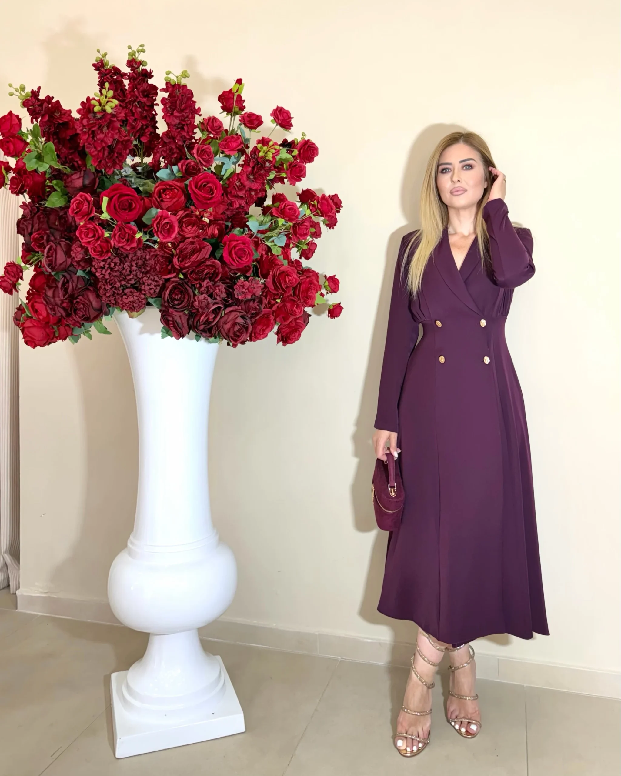 Plum wrap midi dress with gold buttons, metallic strappy heels, and a small matching plum handbag.