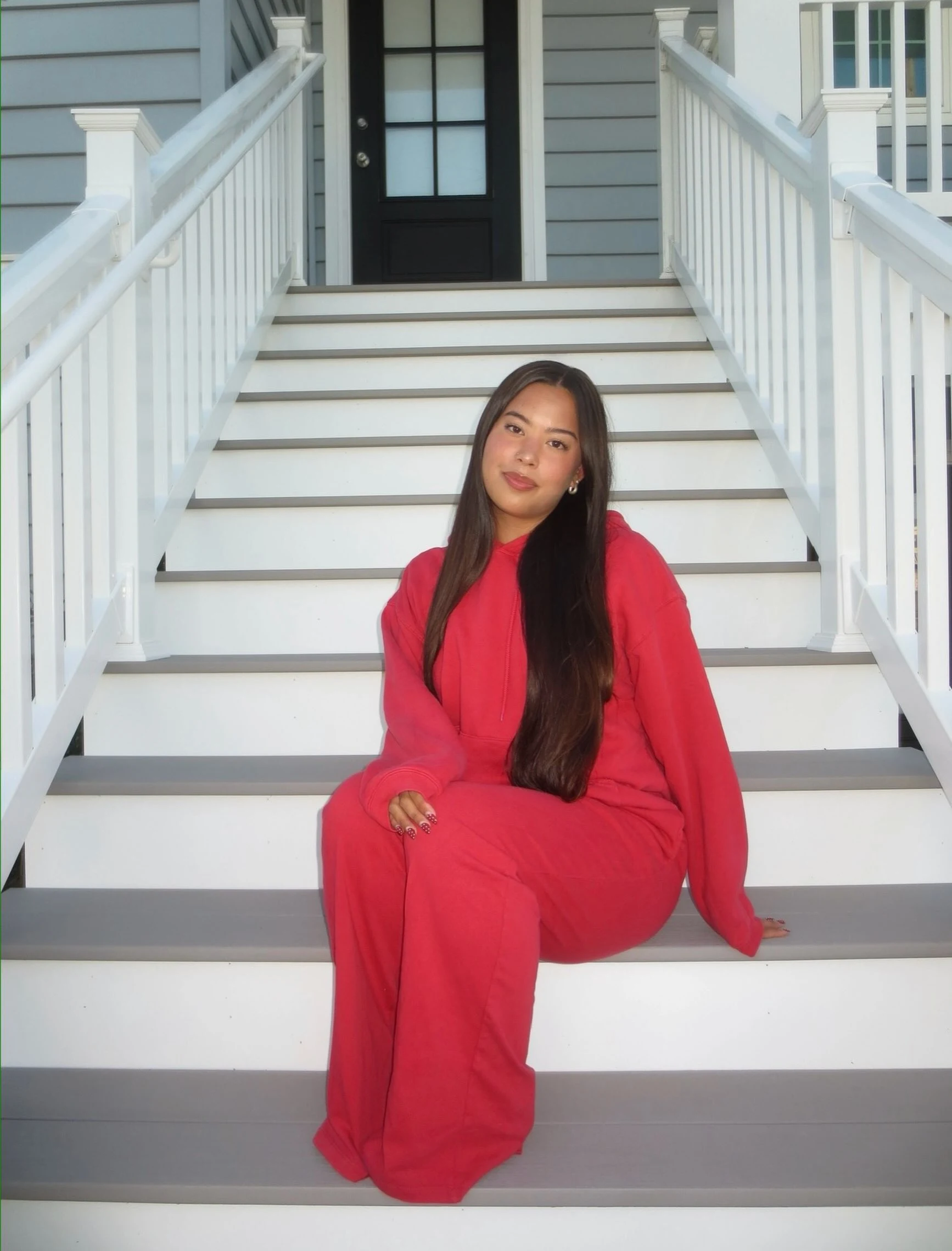 Person in a matching bright red hoodie and wide-leg pants seated on white stairs with gray treads.