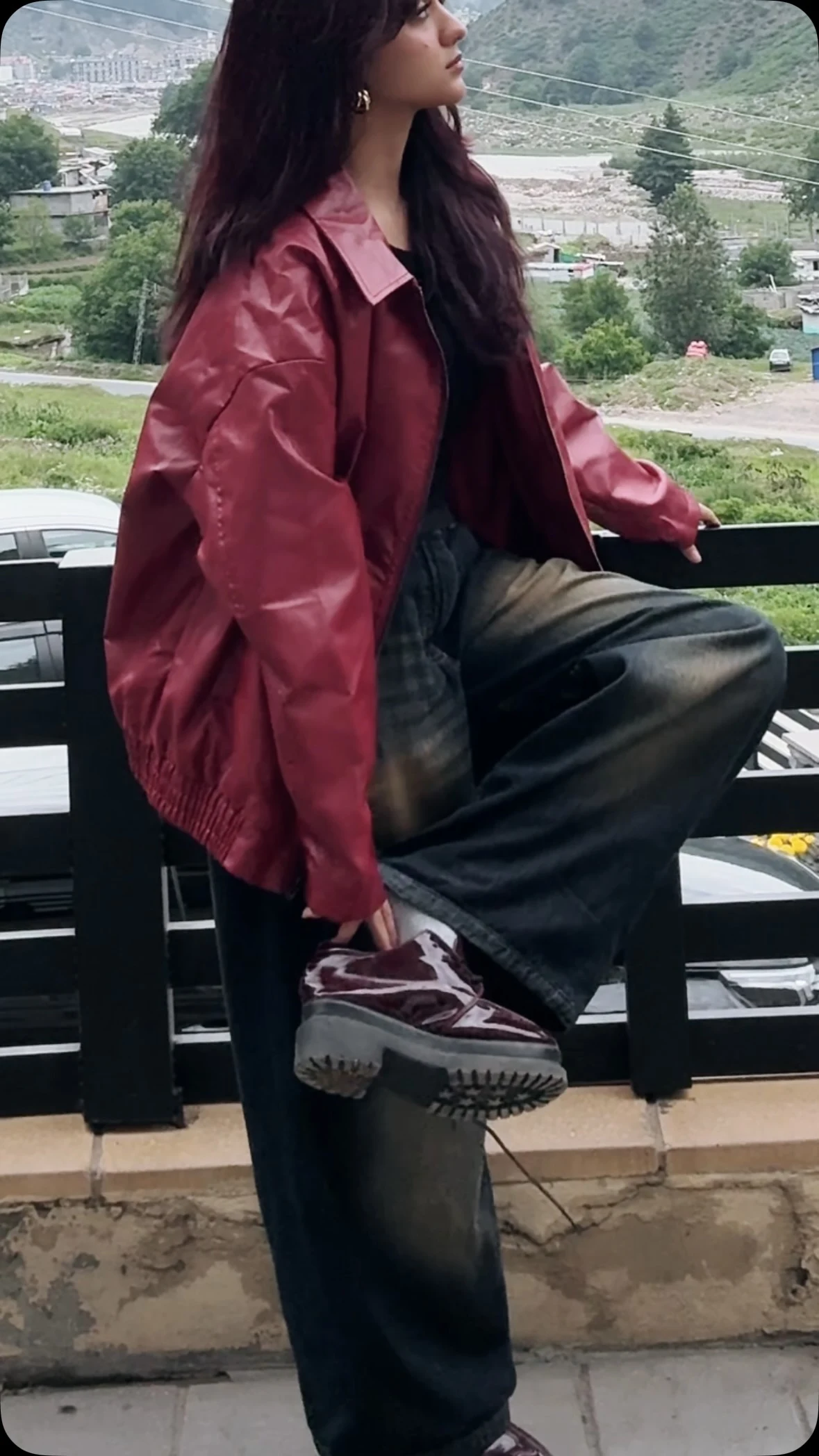 shiny burgundy-red leather bomber jacket, plain black crew-neck top, high-waisted very wide-leg dark jeans with faded thigh panels, chunky dark brown platform loafers