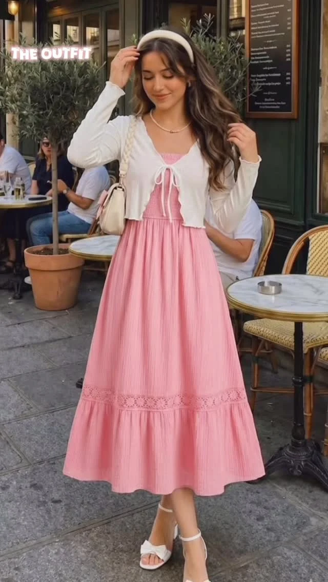 Pink smocked midi dress with lace trim layered under a white cropped cardigan and bow-detailed heels.