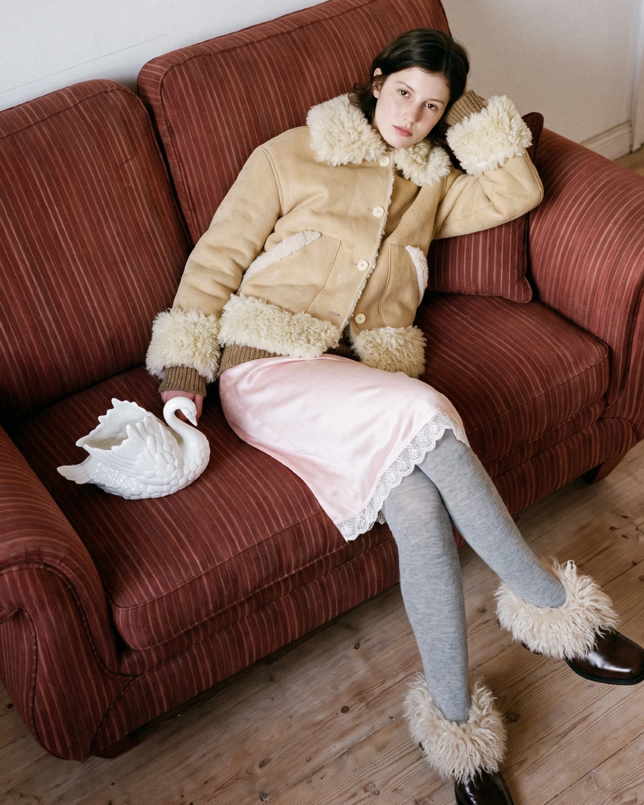 Tan button-front jacket with cream fuzzy trim worn over a pink lace skirt, gray tights, and trimmed shoes.