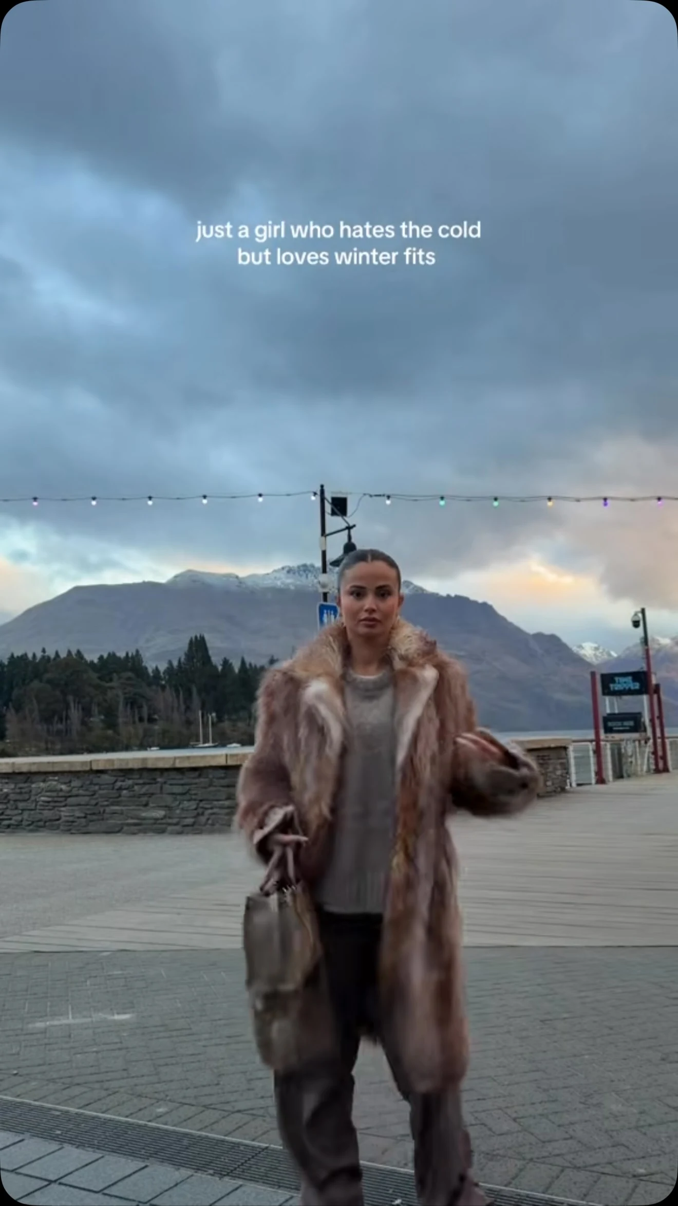 Voluminous long light brown faux fur coat layered over a matching grey knit sweater and trousers.