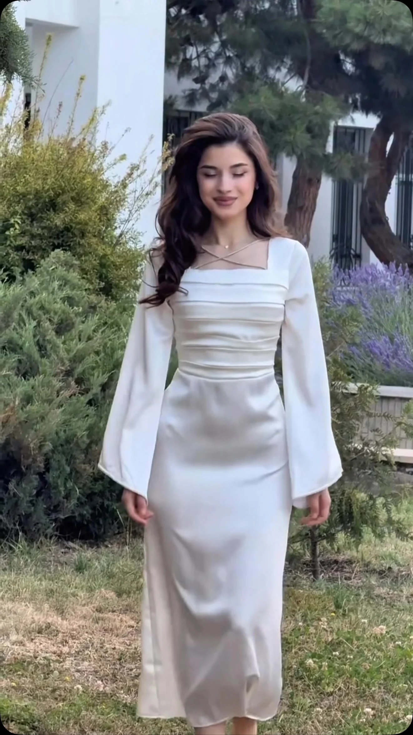 Woman in a white satin floor-length dress with bell sleeves, ruched bodice, and corset lace-up back.