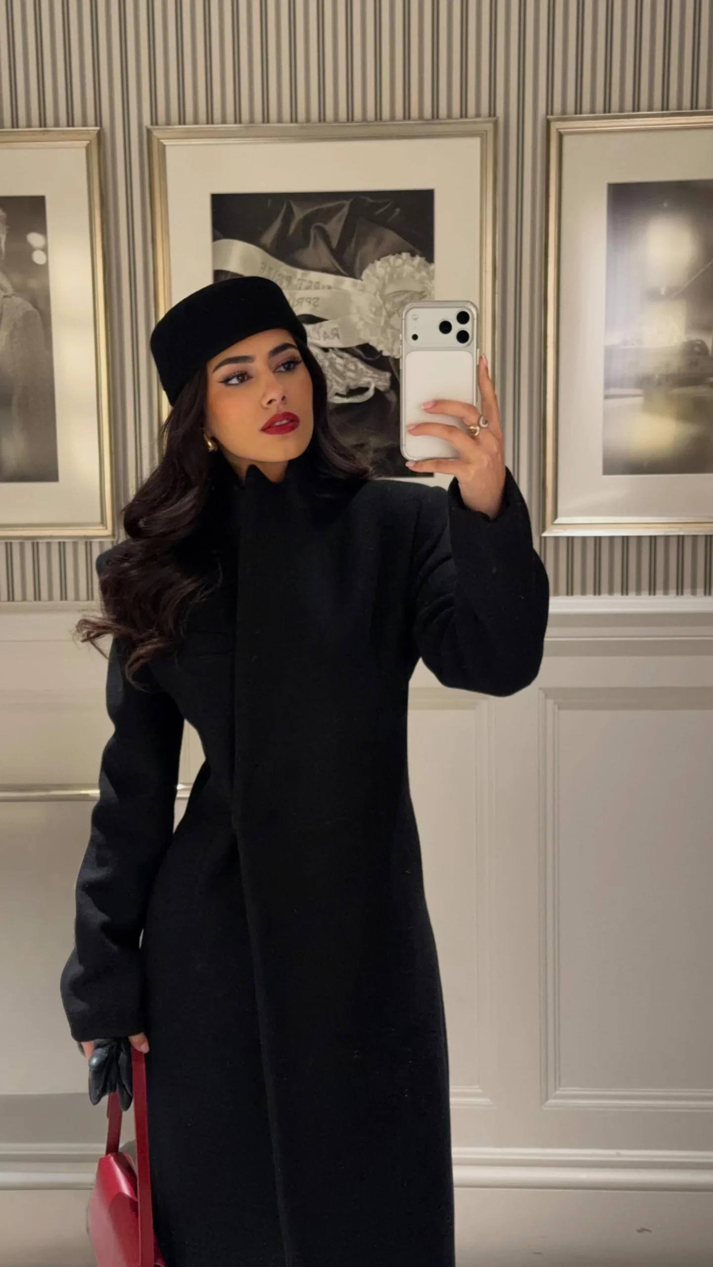 Woman wearing an all-black pantsuit, coat, turtleneck, and pointed-toe heels on a city street.