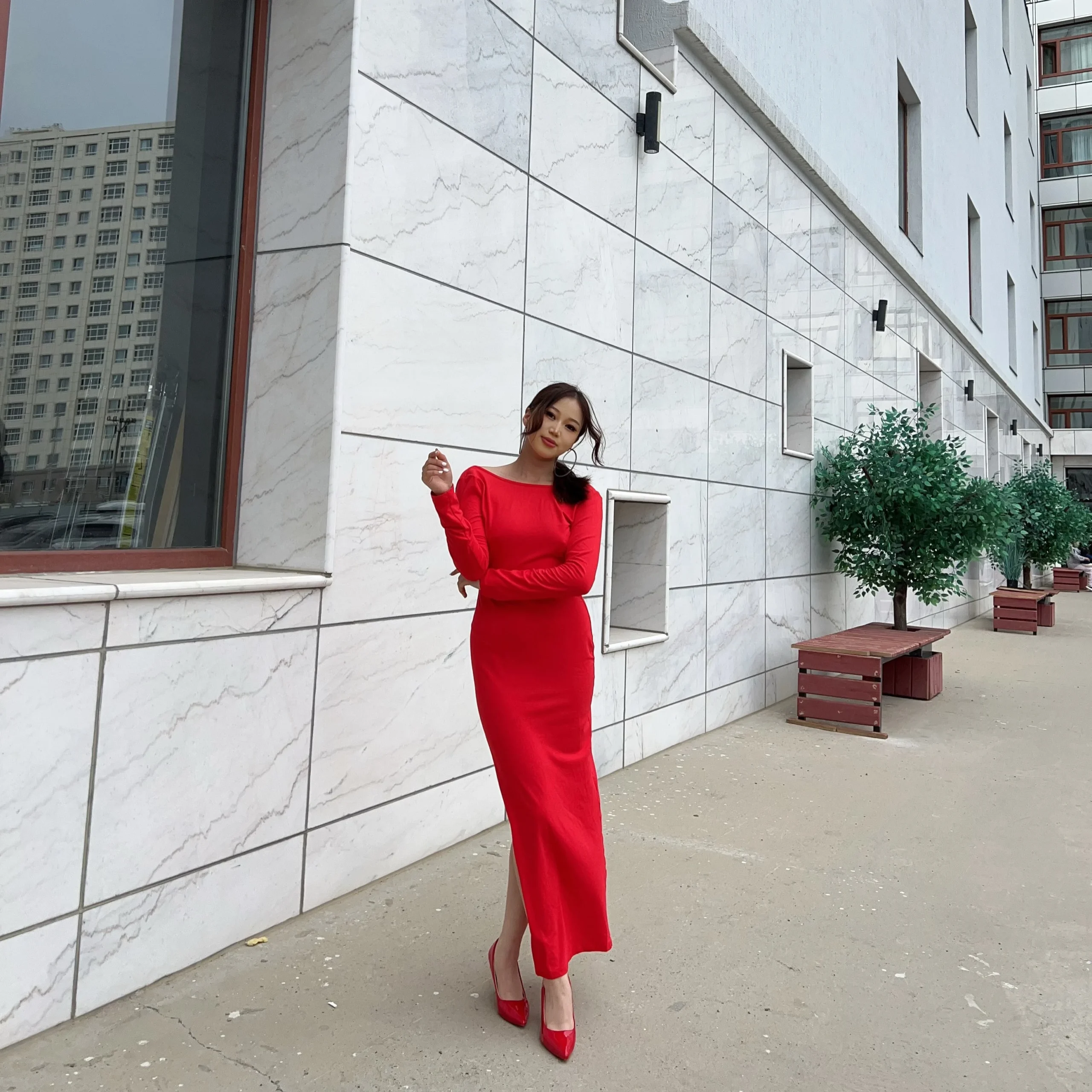 Woman wearing a backless red long-sleeve maxi dress with thigh slit and red stilettos.
