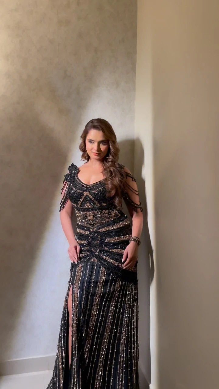 Floor-length black beaded gown with cold-shoulder sleeves, bronze waist bands, and a front slit.