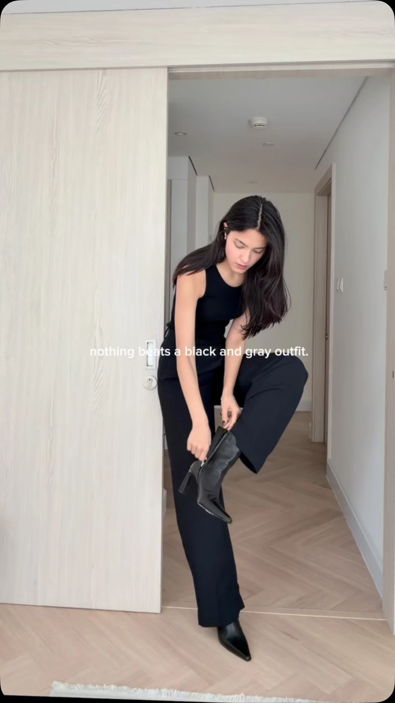 All-black outfit with wide-leg trousers, gray knit jumper, and pointed ankle boots.