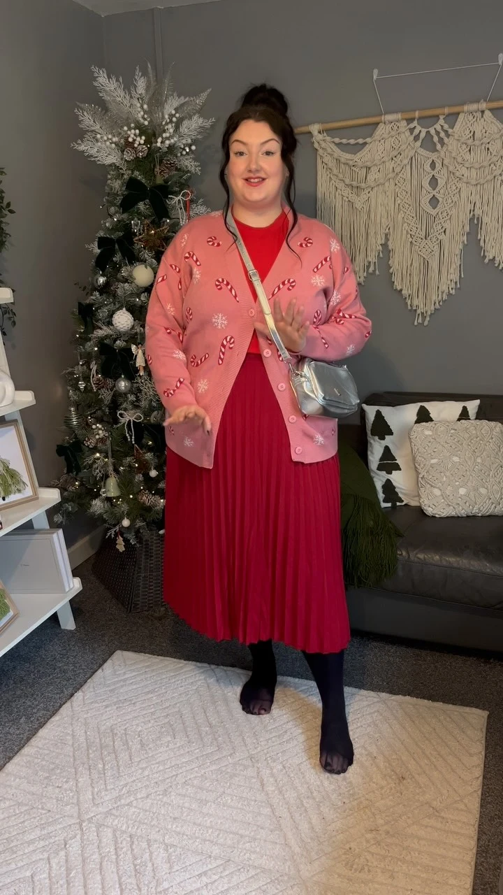 Pink candy cane cardigan layered over a red pleated maxi dress with dark tights and silver crossbody bag.