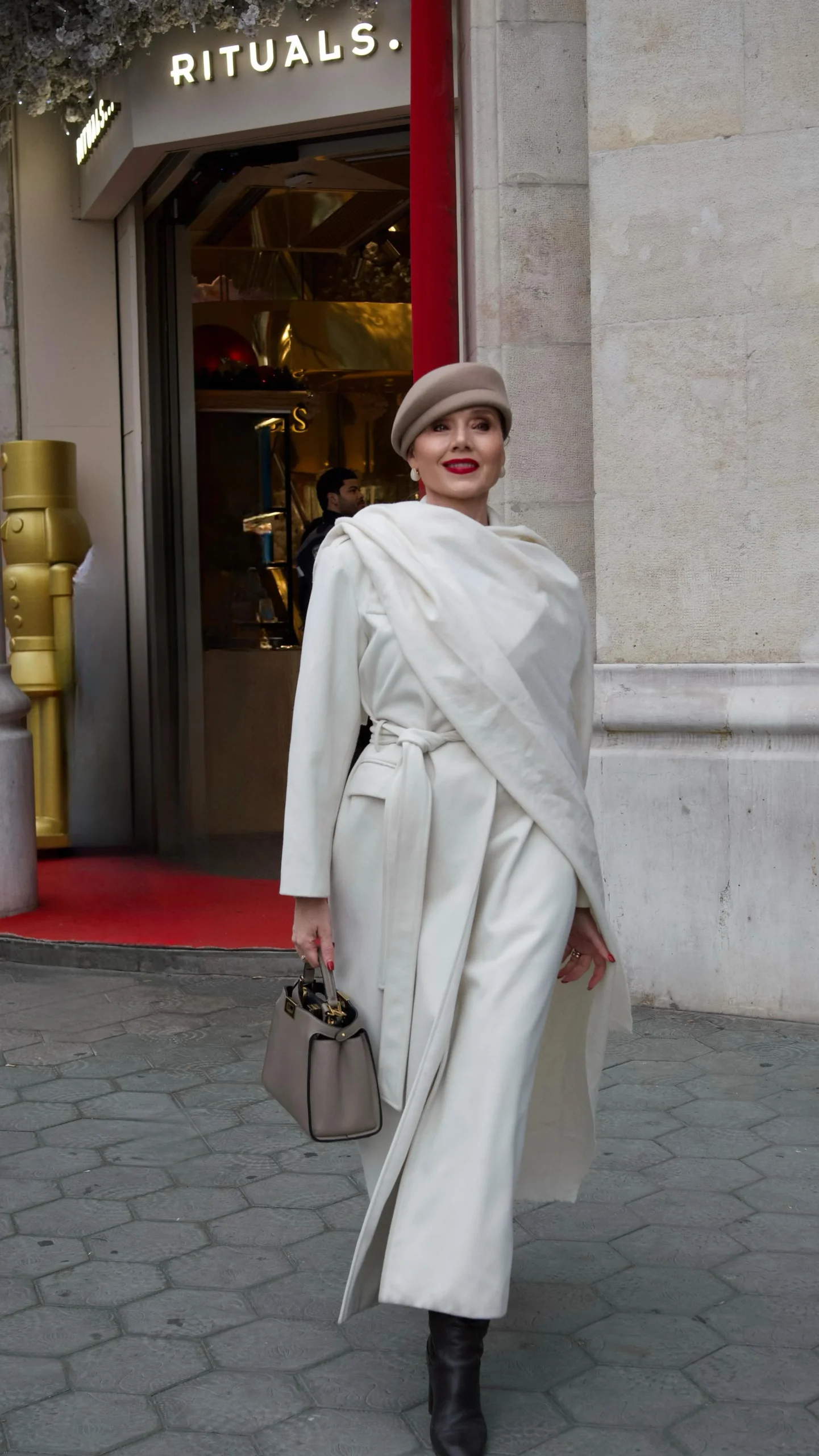 Long cream wrap coat with wide collar, black turtleneck, black wide-leg trousers, black pointed-toe boots