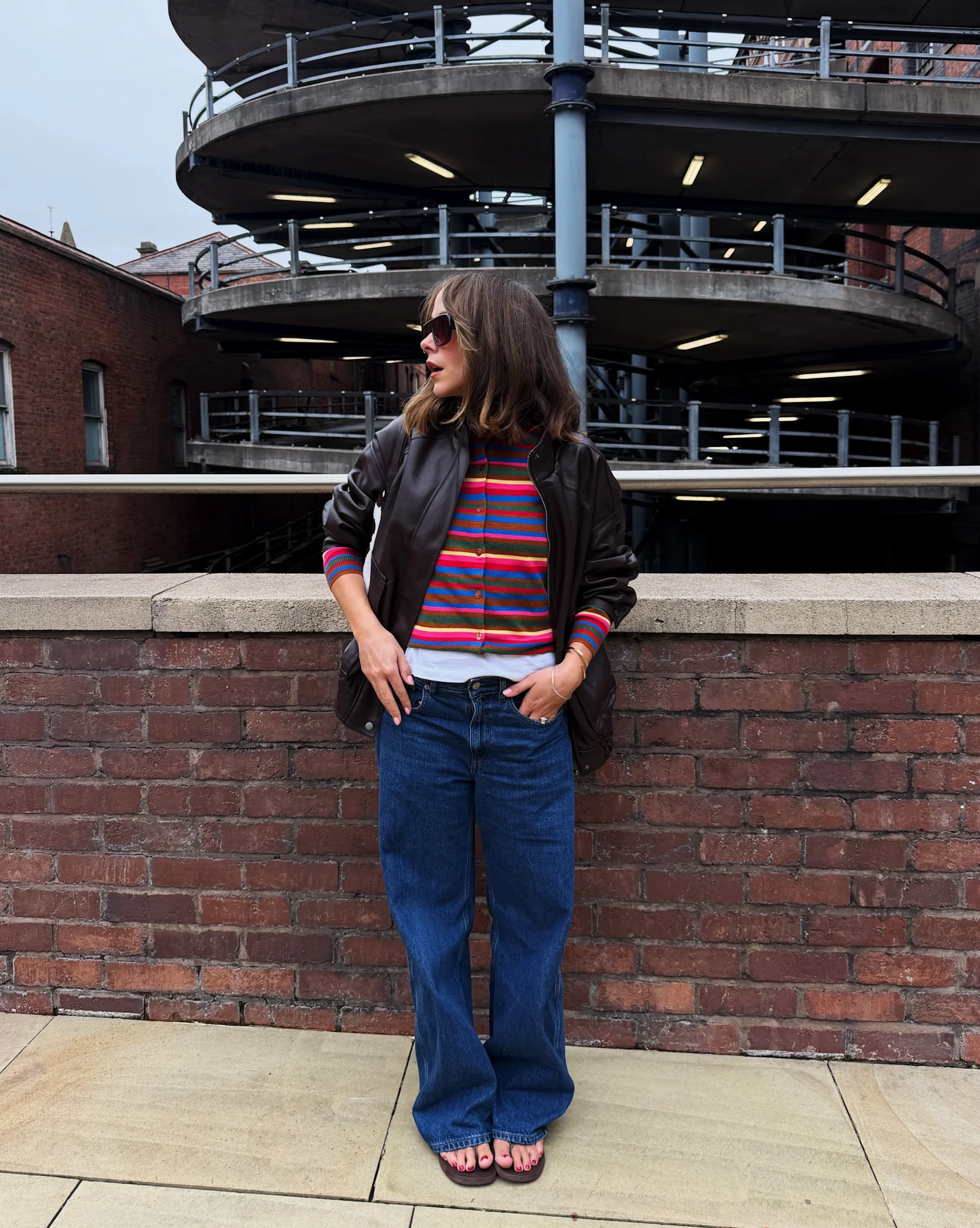 Dark brown leather bomber over brown cardigan and blue wide-leg jeans outfit.