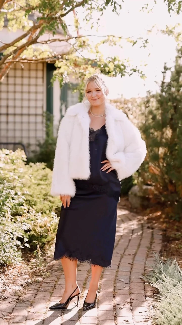 Navy lace-trimmed slip dress with cropped white faux fur jacket and black pointed-toe heels.
