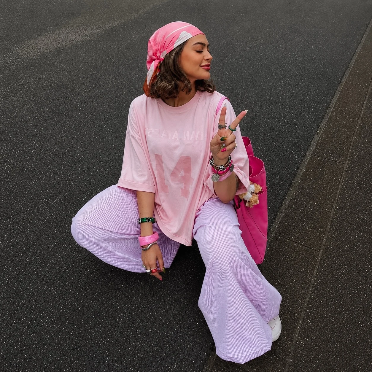 Oversized pink graphic tee paired with lavender checked flared trousers, pink headscarf, and bright pink bag.