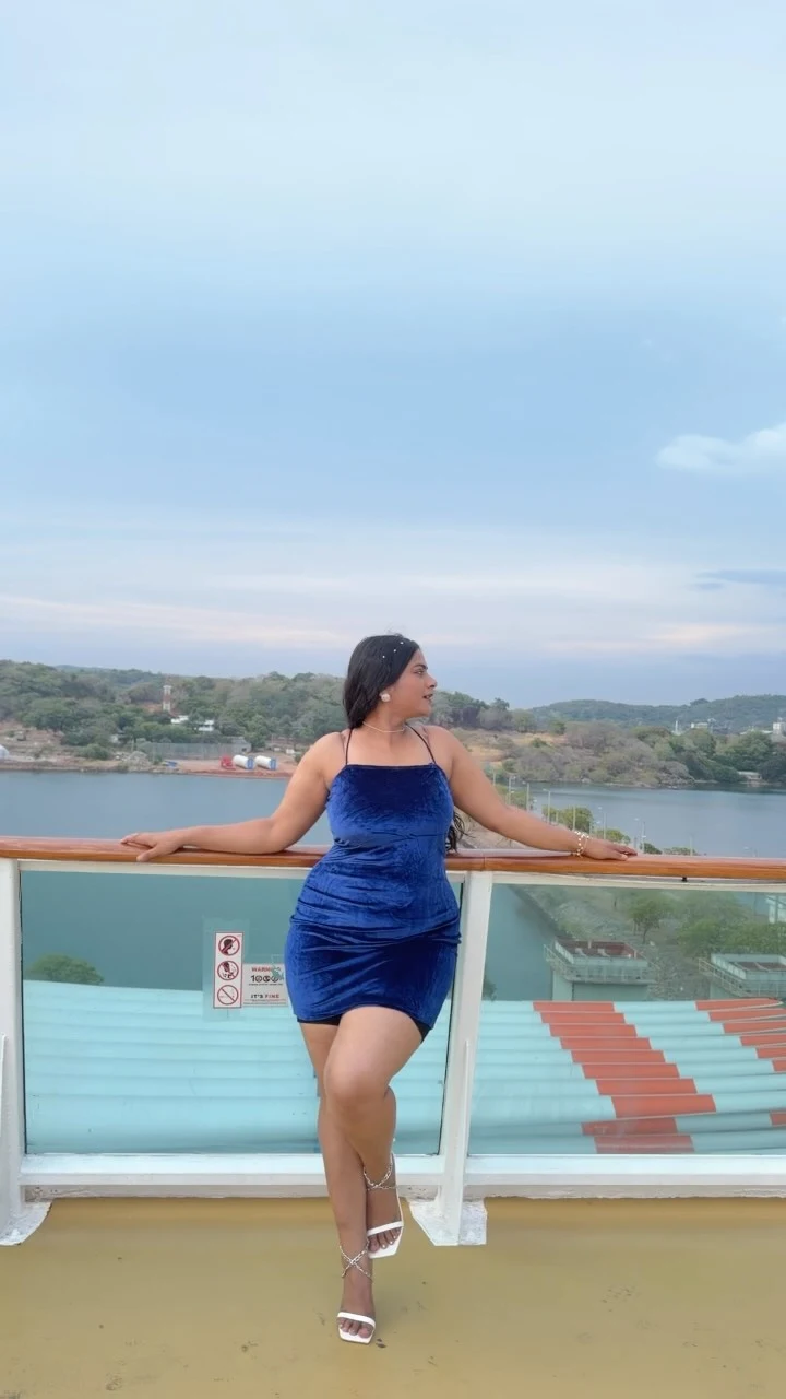 Woman wearing a royal blue velvet spaghetti-strap mini dress and white strappy heeled sandals.