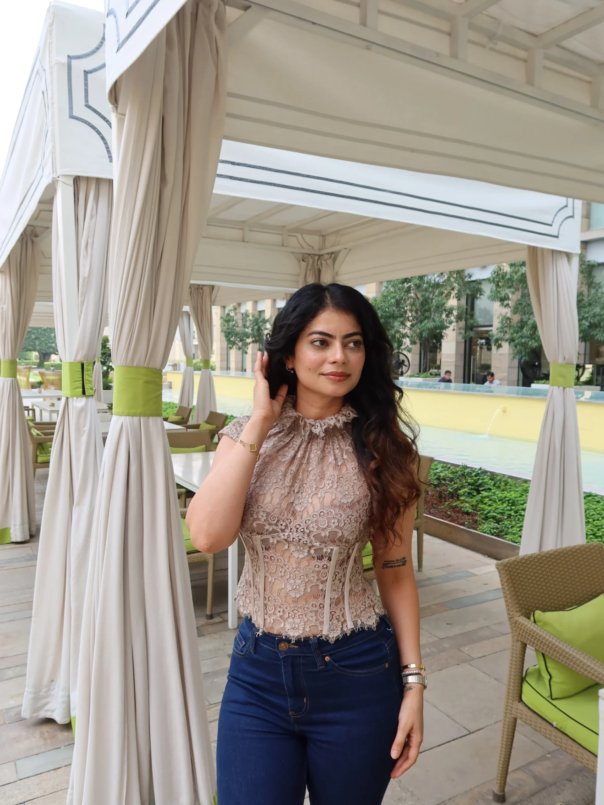 Woman in a sheer beige lace corset top and dark blue high-waisted jeans.